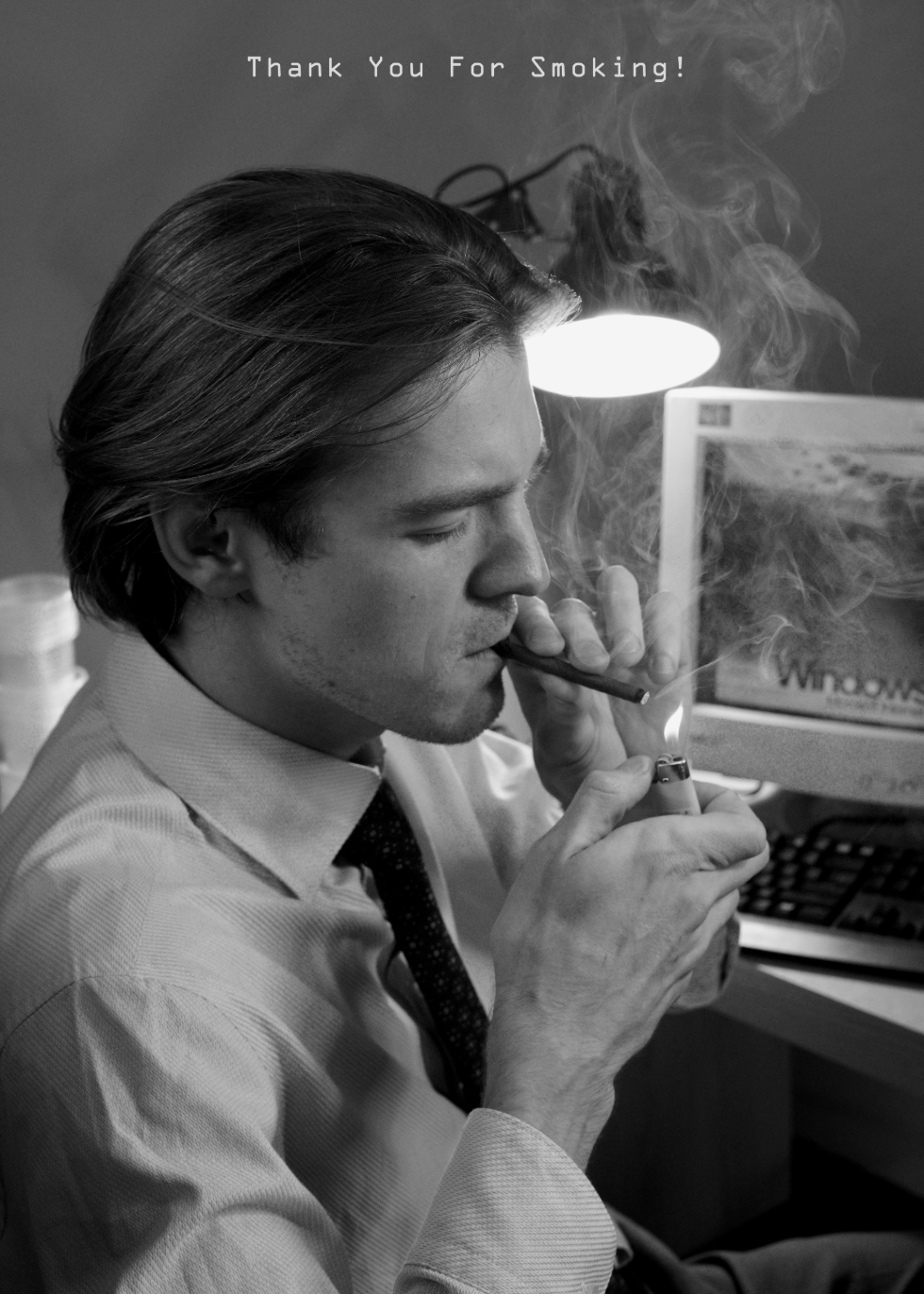 A man in a shirt and tie is smoking a cigar at a desk with a computer monitor in the background. The image is in black and white, and a message at the top reads 'Thank You For Smoking!'