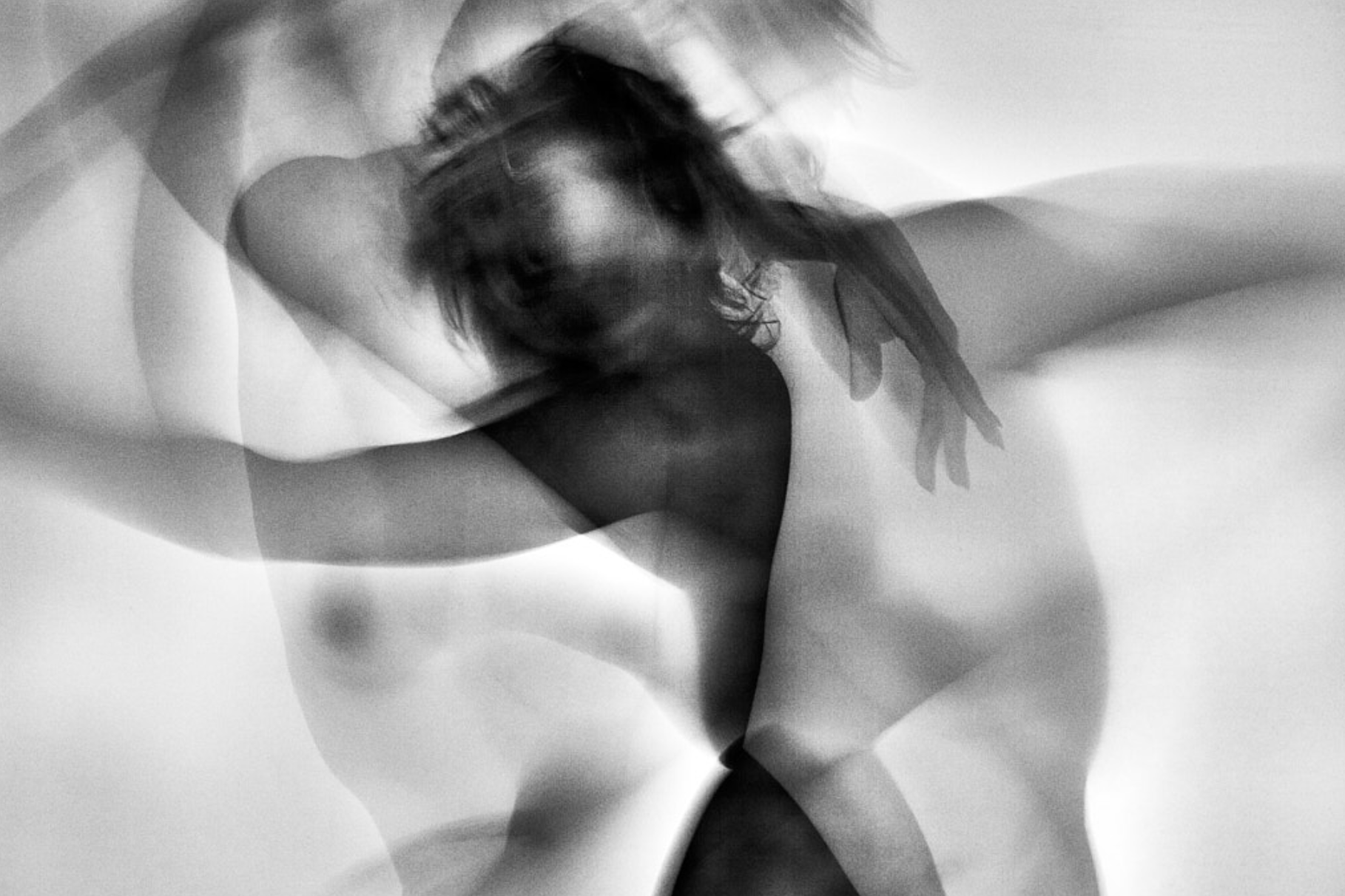 A black and white abstract photograph of a woman with long, wavy hair, her face partially visible, with blurred motion and overlapping shapes.