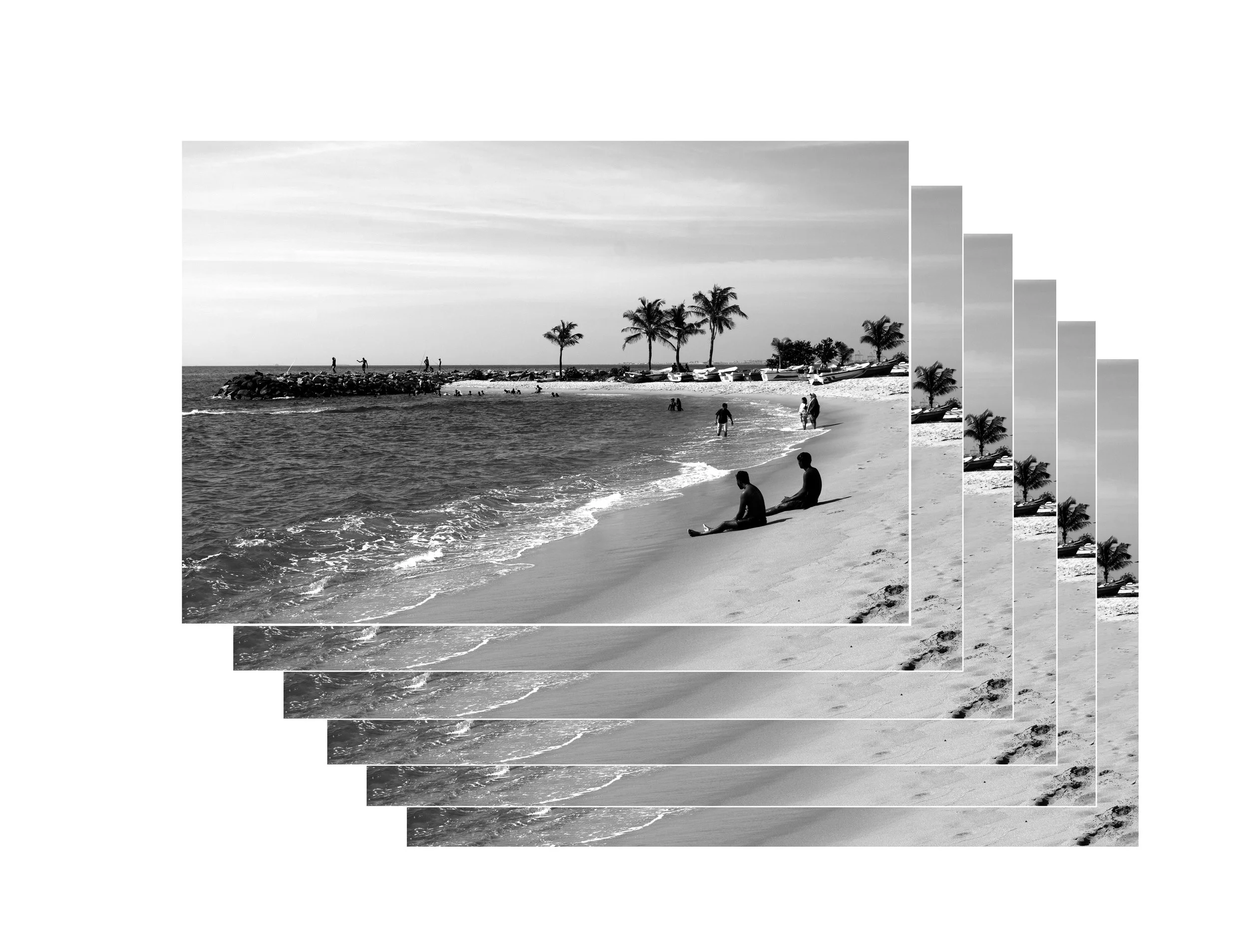Black and white photo of a beach scene with people walking along the shoreline, palm trees, boats on the sand, and a rocky pier extending into the water.