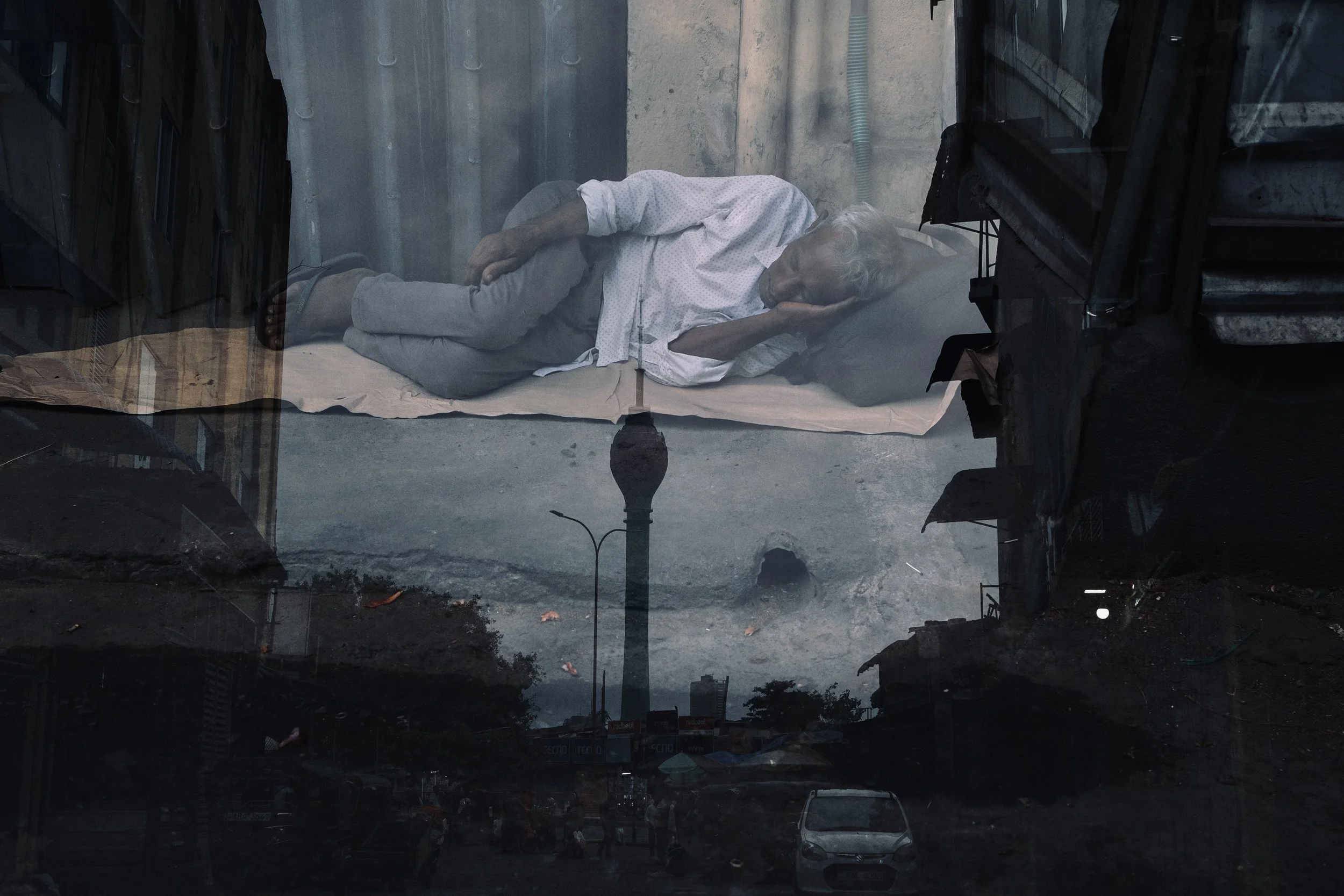 A reflection of a street scene with cars and trees, overlaid with an image of an elderly man lying on a bed inside a building, appearing to be sleeping or resting.