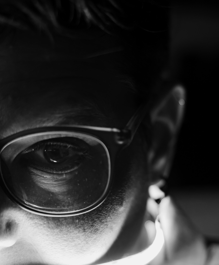 Close-up of a person wearing glasses, showing one eye and part of their face in black and white.