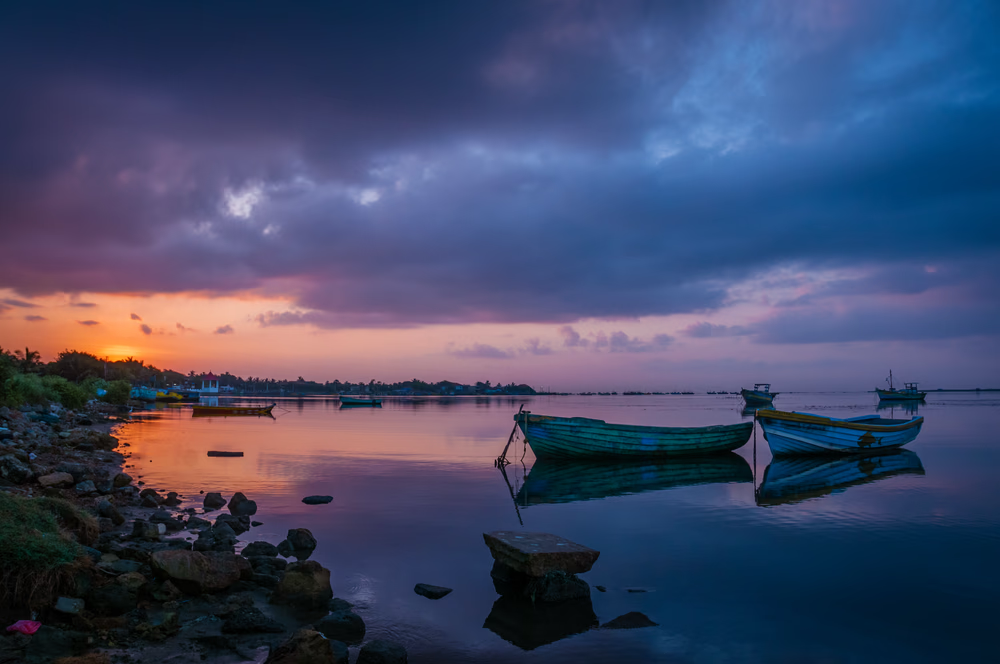 Boats anchored on a calm shoreline during sunset with a partly cloudy sky