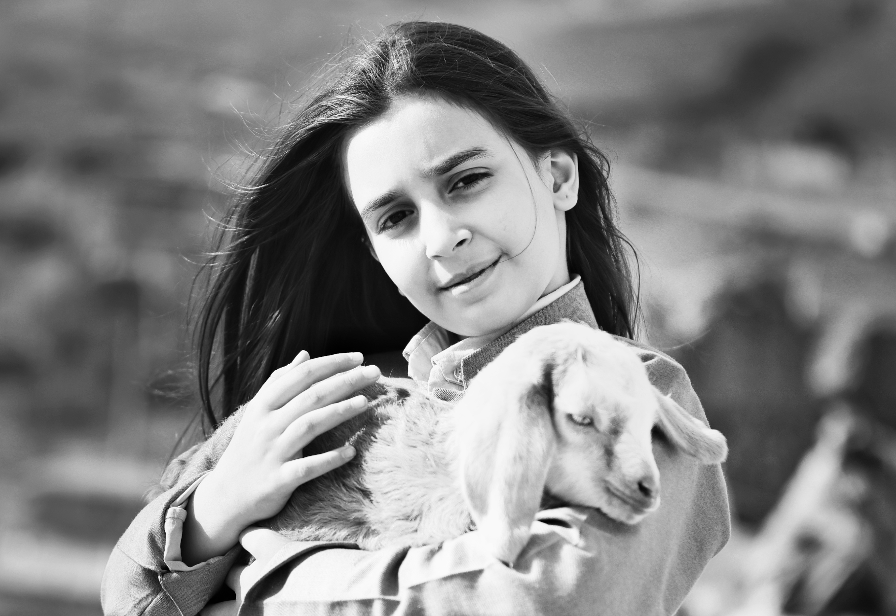 A young woman with long dark hair holding a sleeping puppy outdoors. The photo is in black and white.