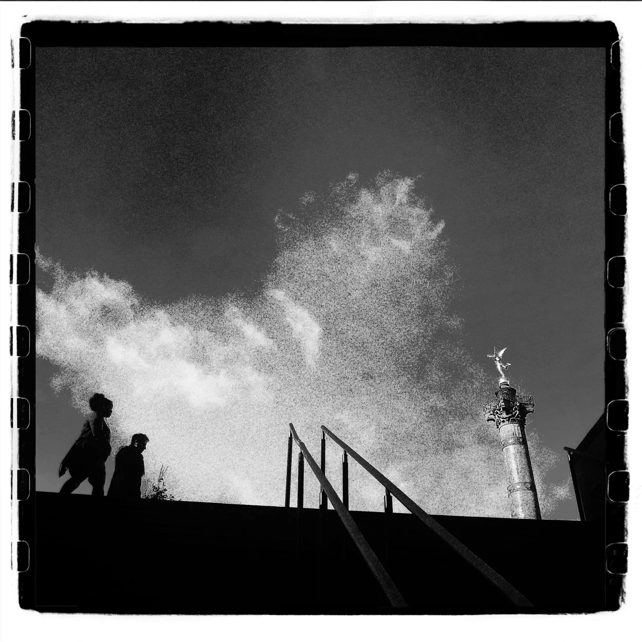 Black and white photograph of three silhouettes of people walking up stairs, with a smokestack emitting smoke or steam in the background, and a hazy sky.