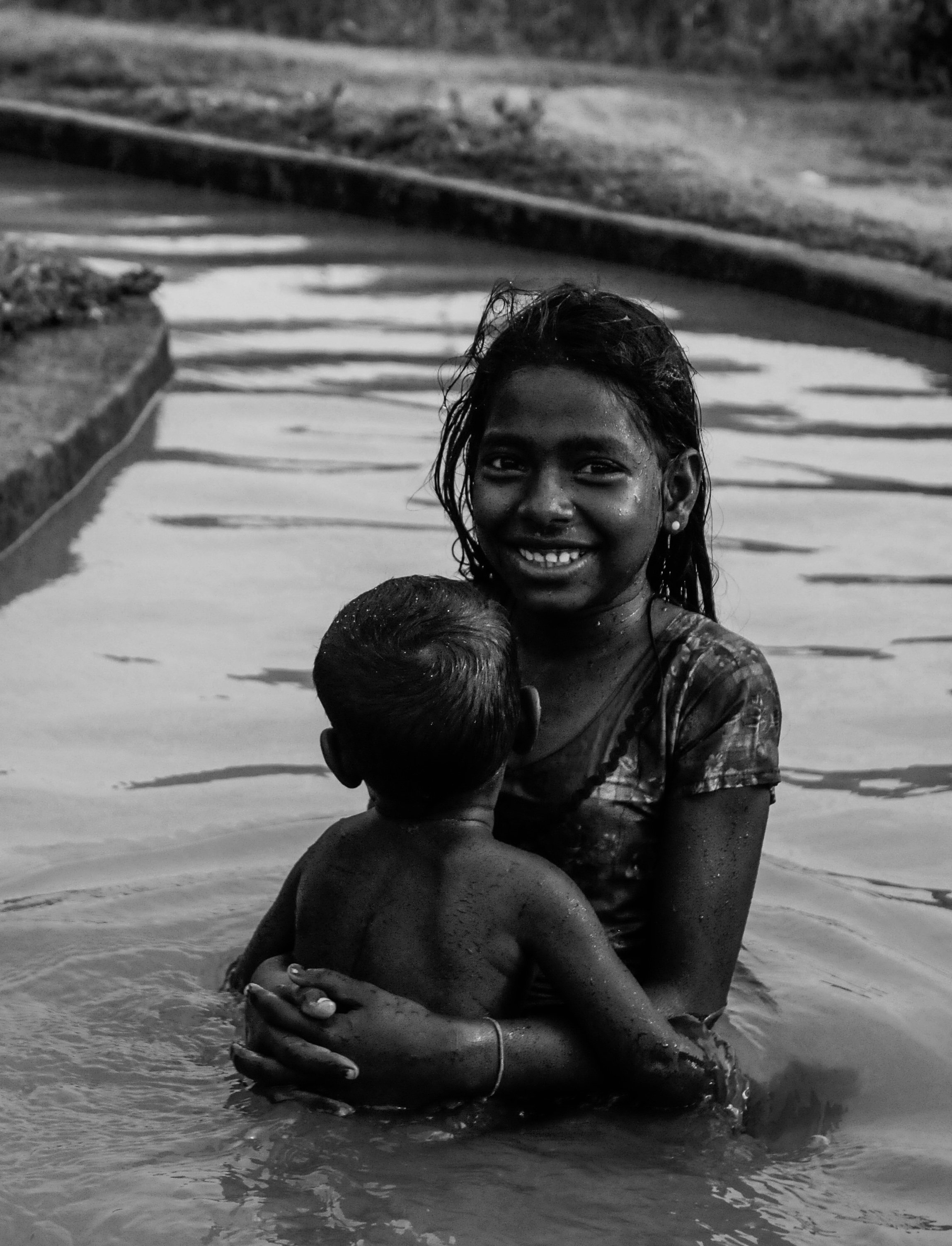 A woman smiling in a river, holding a young child with wet hair and skin, during daytime.
