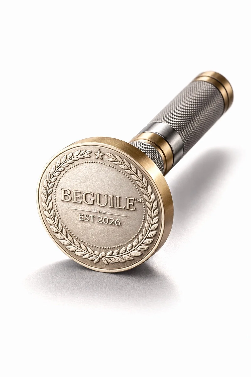 A gold-colored medal with the word 'BEGUILE' engraved, surrounded by a laurel wreath, with 'EST 2026' inscribed below, attached to a textured metallic handle.