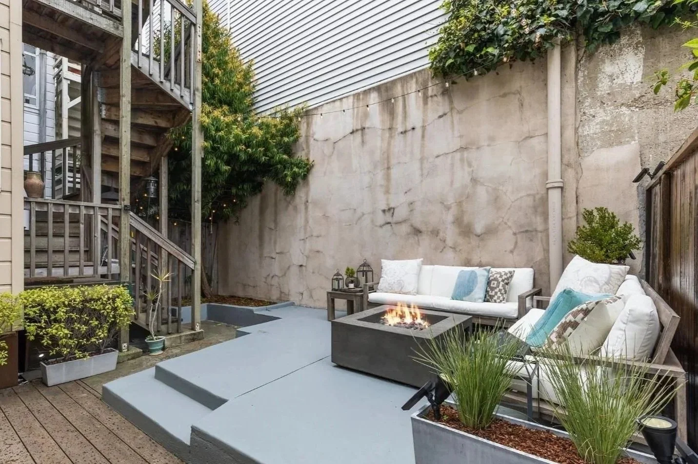 An outdoor patio with sofas, a fire pit, potted plants, and string lights.