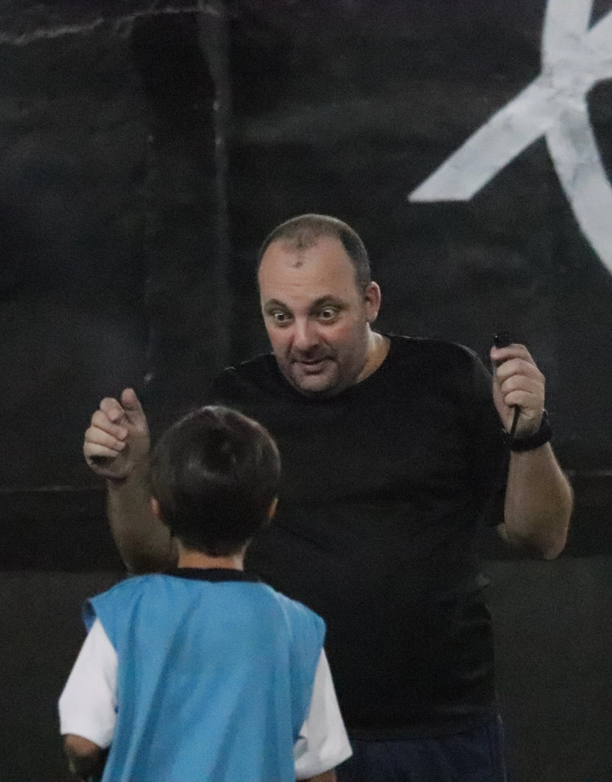 Homem com expressão animada falando com criança de costas, em ambiente interno.