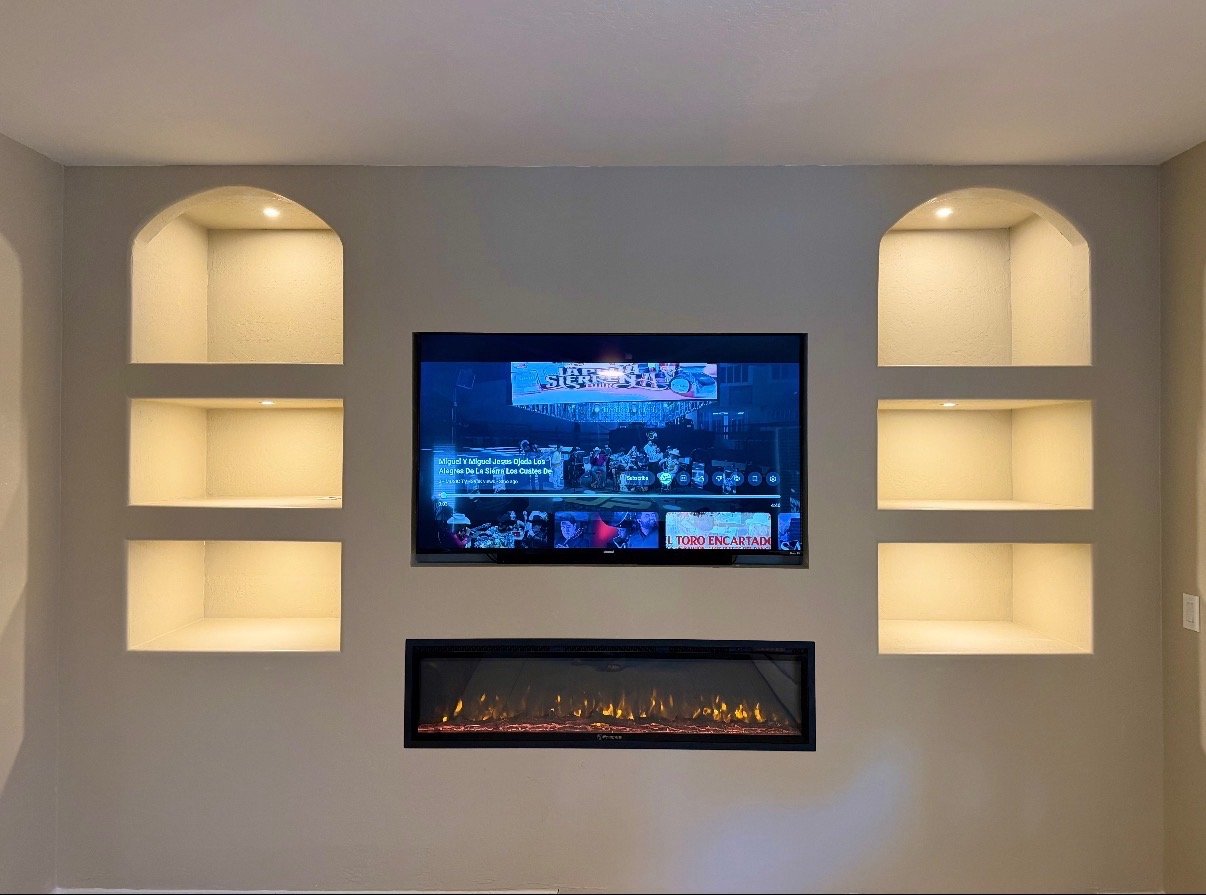 Living room wall with built-in shelves on each side, a flat-screen TV in the center, and a modern electric fireplace below the TV.