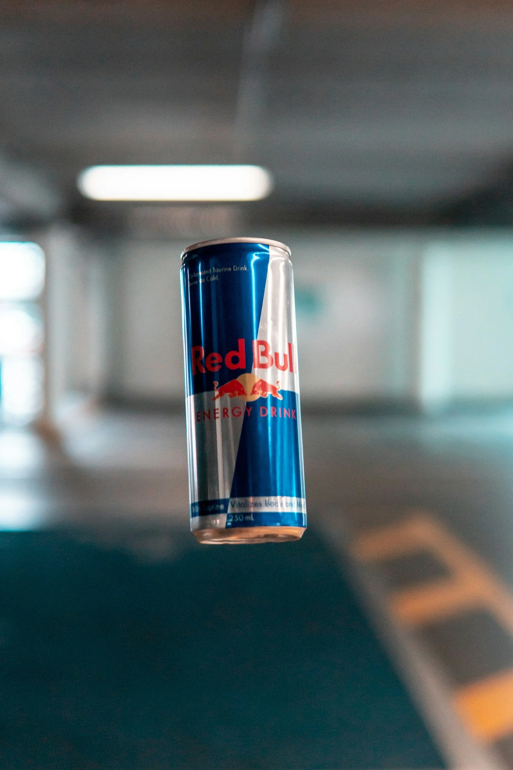Bright red neon Red Bull logo with two red bulls charging at each other in front of a yellow circle, against a dark background, illuminated with blue and purple light reflections.