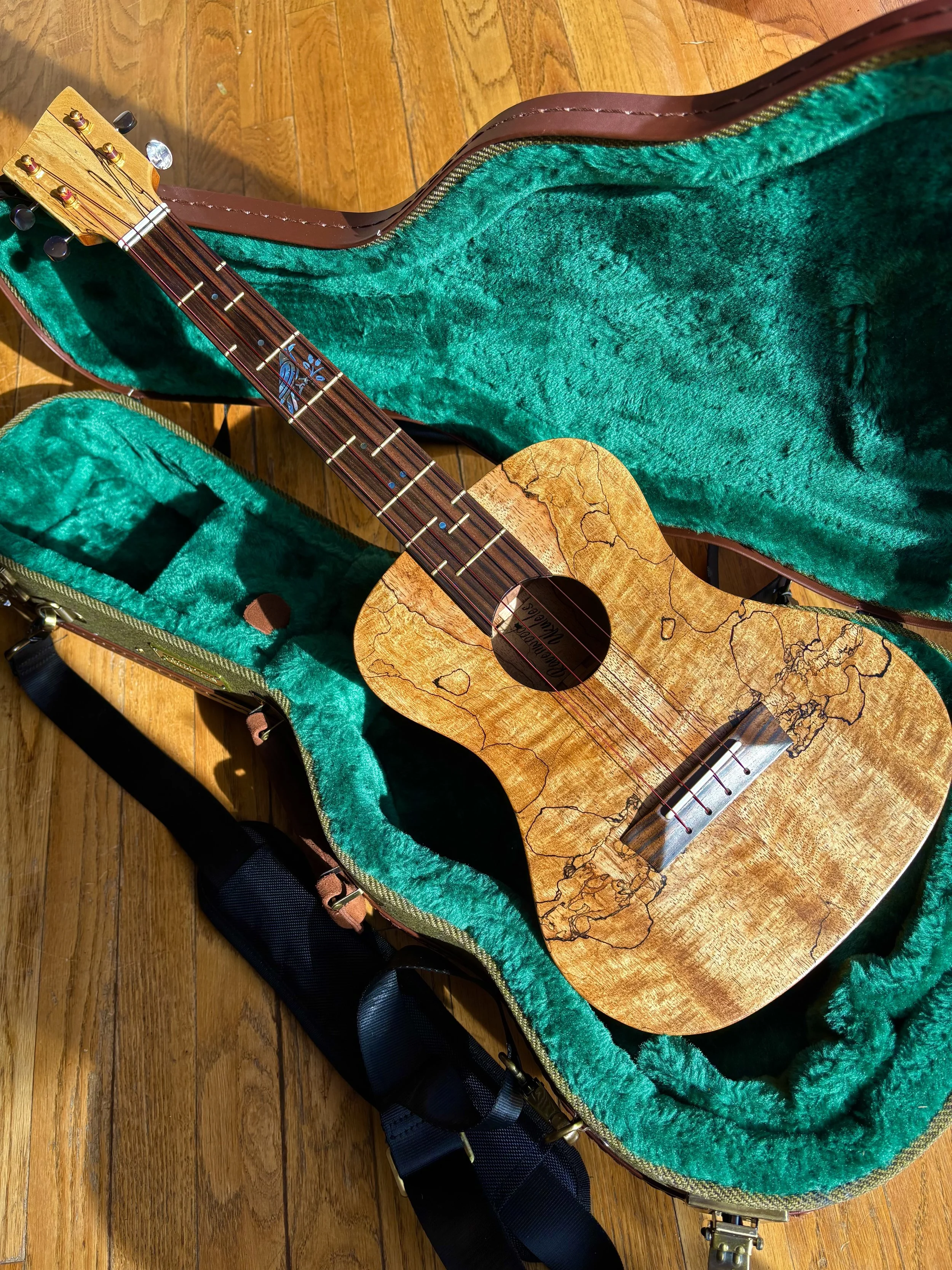 An acoustic guitar with a wood grain finish rests inside an open green plush-lined hard case on a wooden floor.