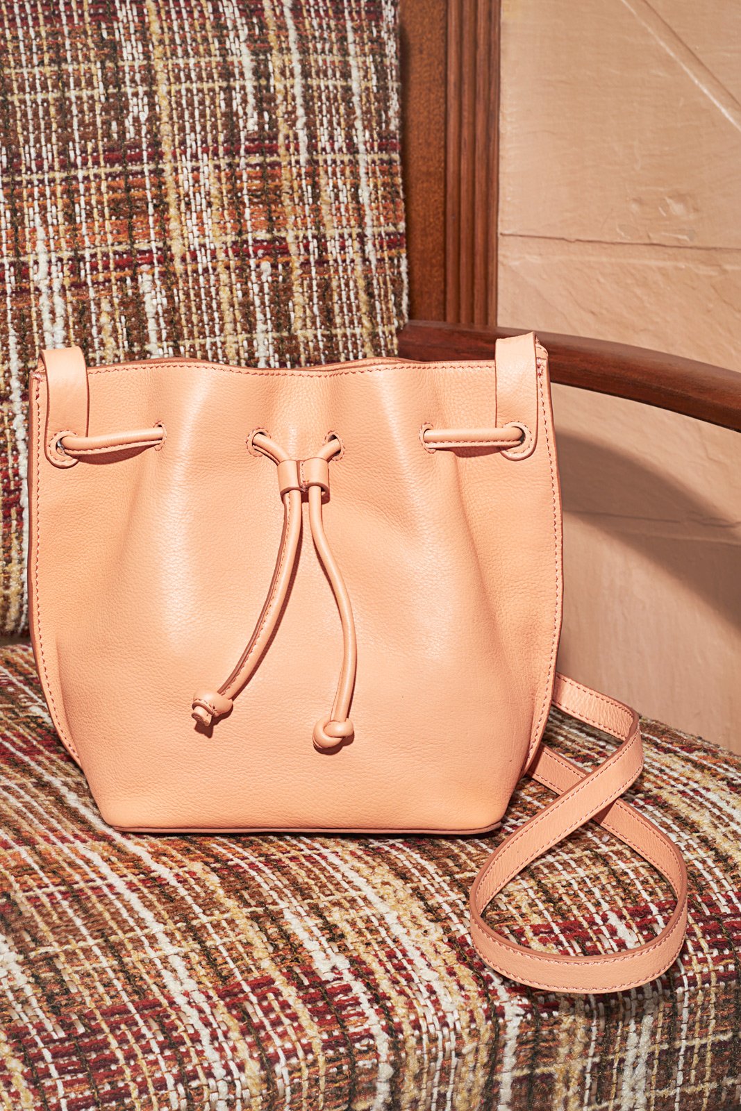 A peach-colored leather handbag with a drawstring and strap, resting on a patterned upholstery chair.