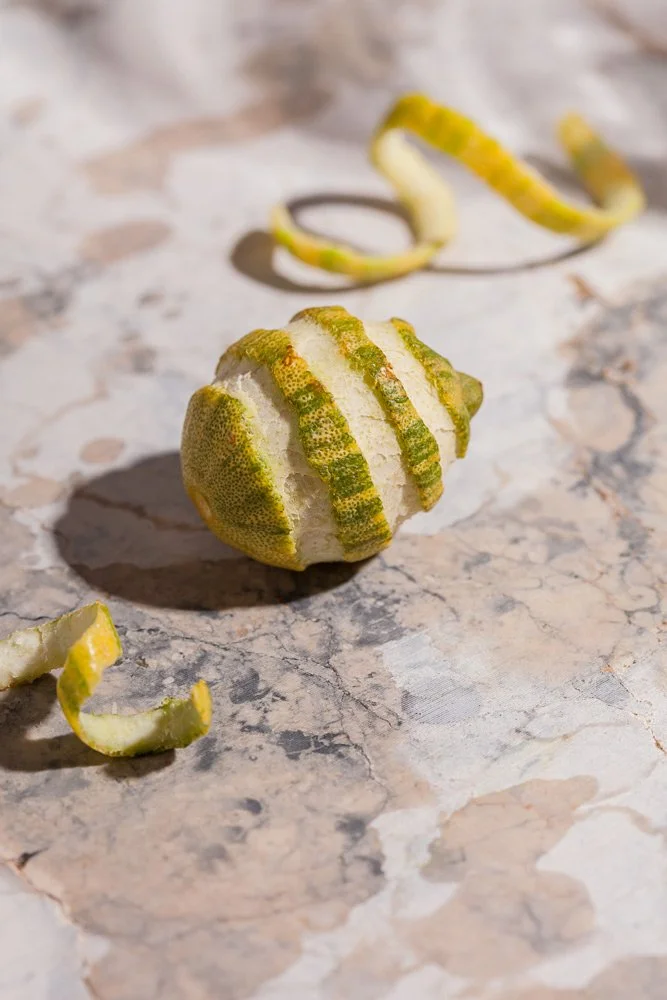 A lemon partially peeled with its peel curled on a marble surface.