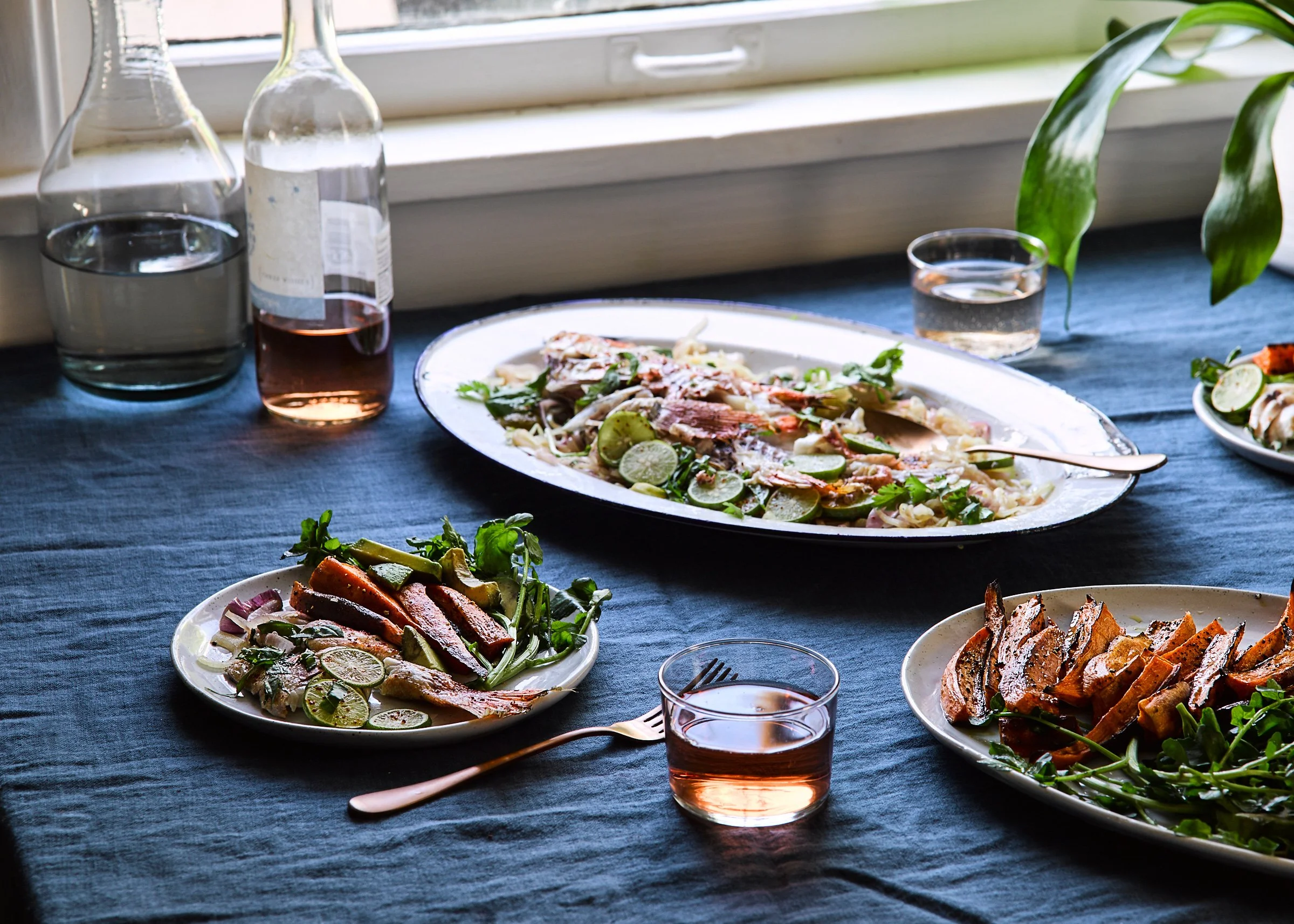 platter holding roasted fish and vegetables on a table with glasses, a wine bottle, and plates of food
