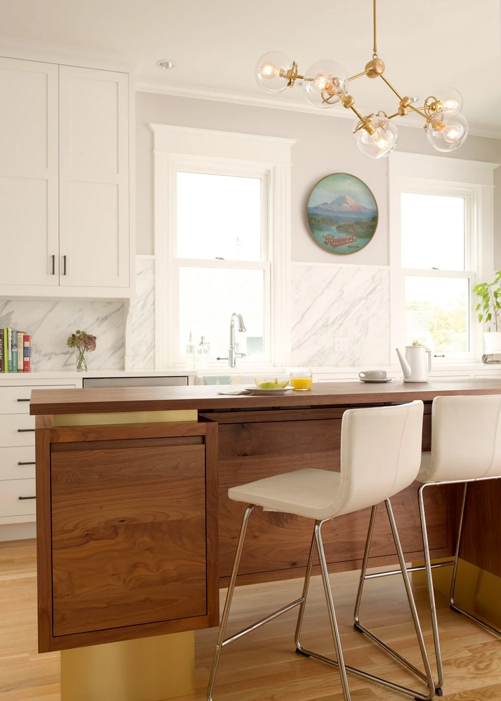 Modern kitchen with white cabinets, marble backsplash, wooden island, two white bar stools, a hanging light fixture, and windows with white trim.