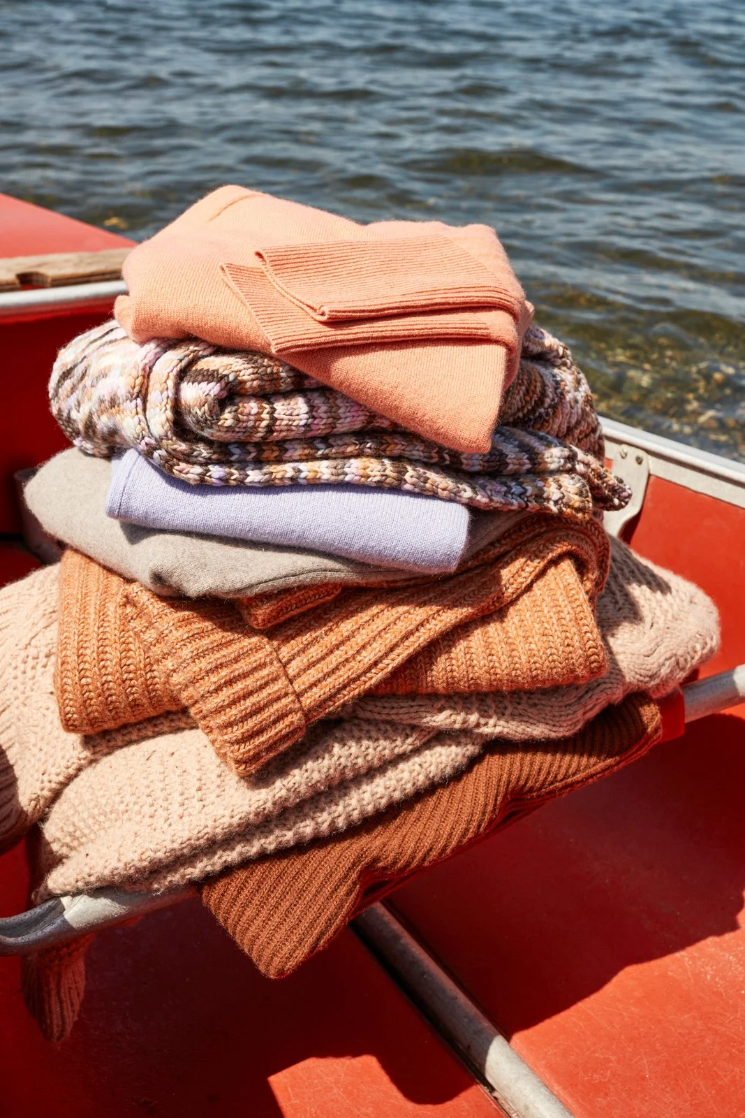 Stack of folded winter clothes, including sweaters and scarves, on a boat with water in the background.