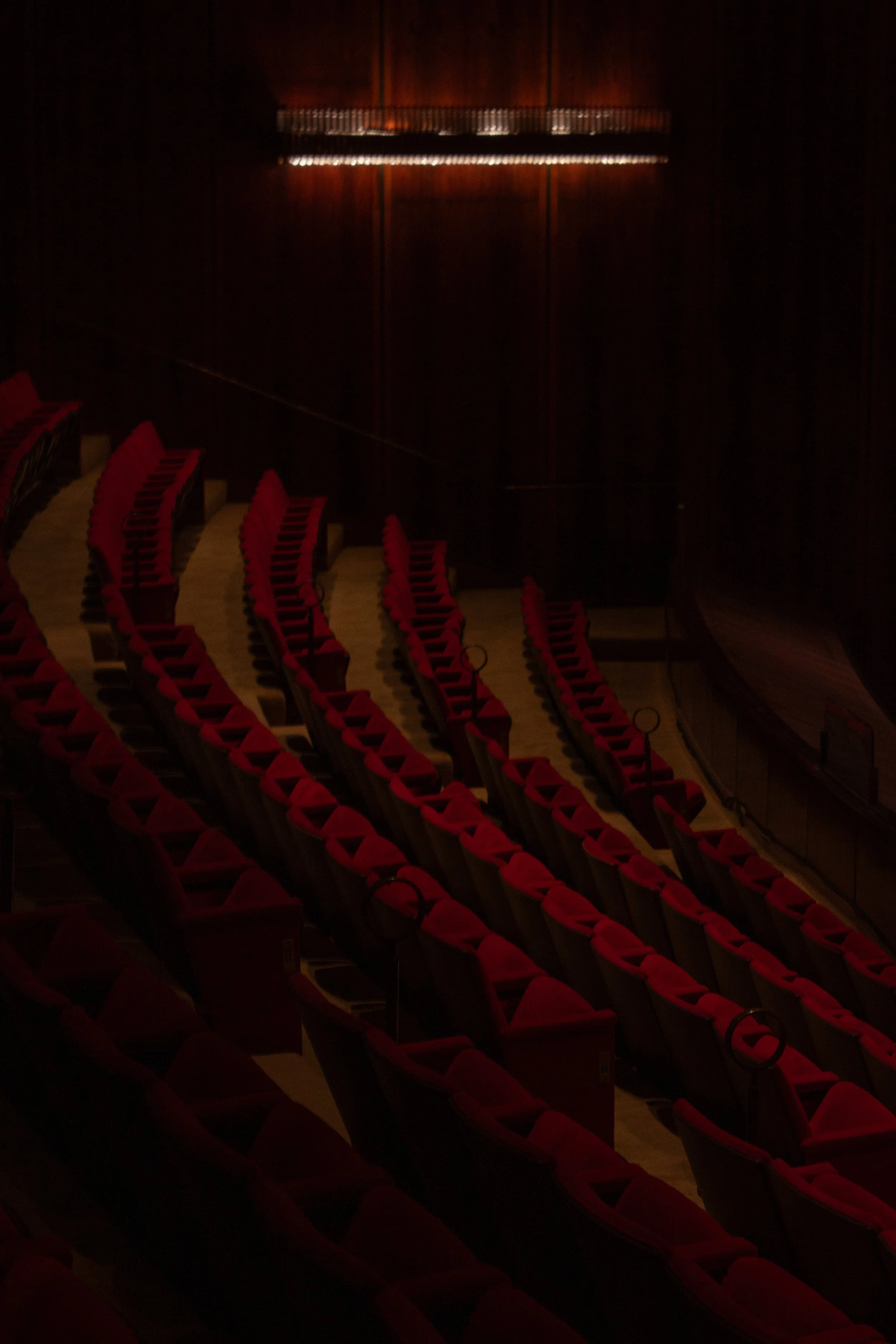 Empty theater auditorium with red seats and dark wood walls.