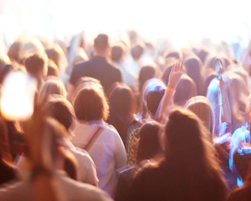Large crowd at an event or concert with raised hands and colorful lighting, similar to the energy and momentum of a SecondActWomen gathering.