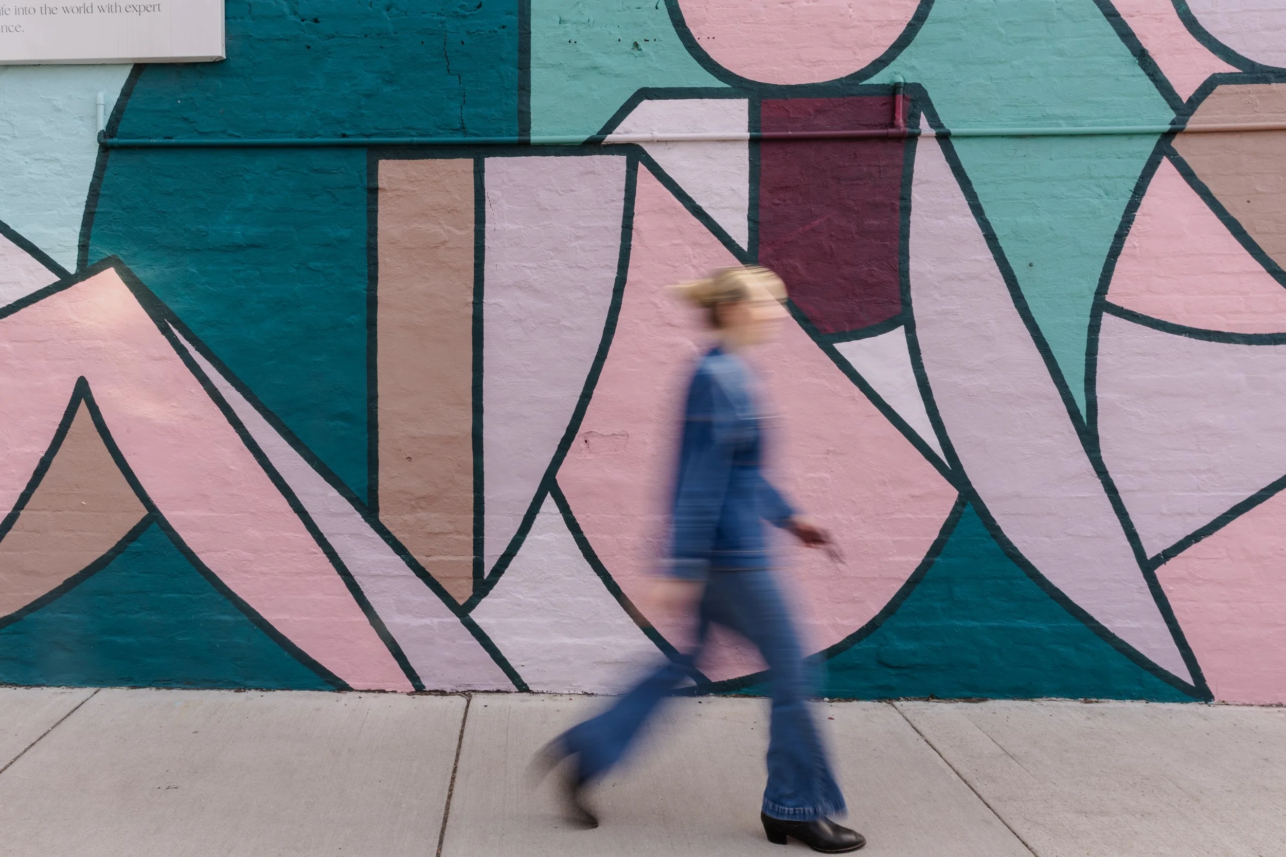 A backyard with a swimming pool, three lounge chairs, and a house with a patio, surrounded by trees and shrubs, in a hilly landscape at sunset.
