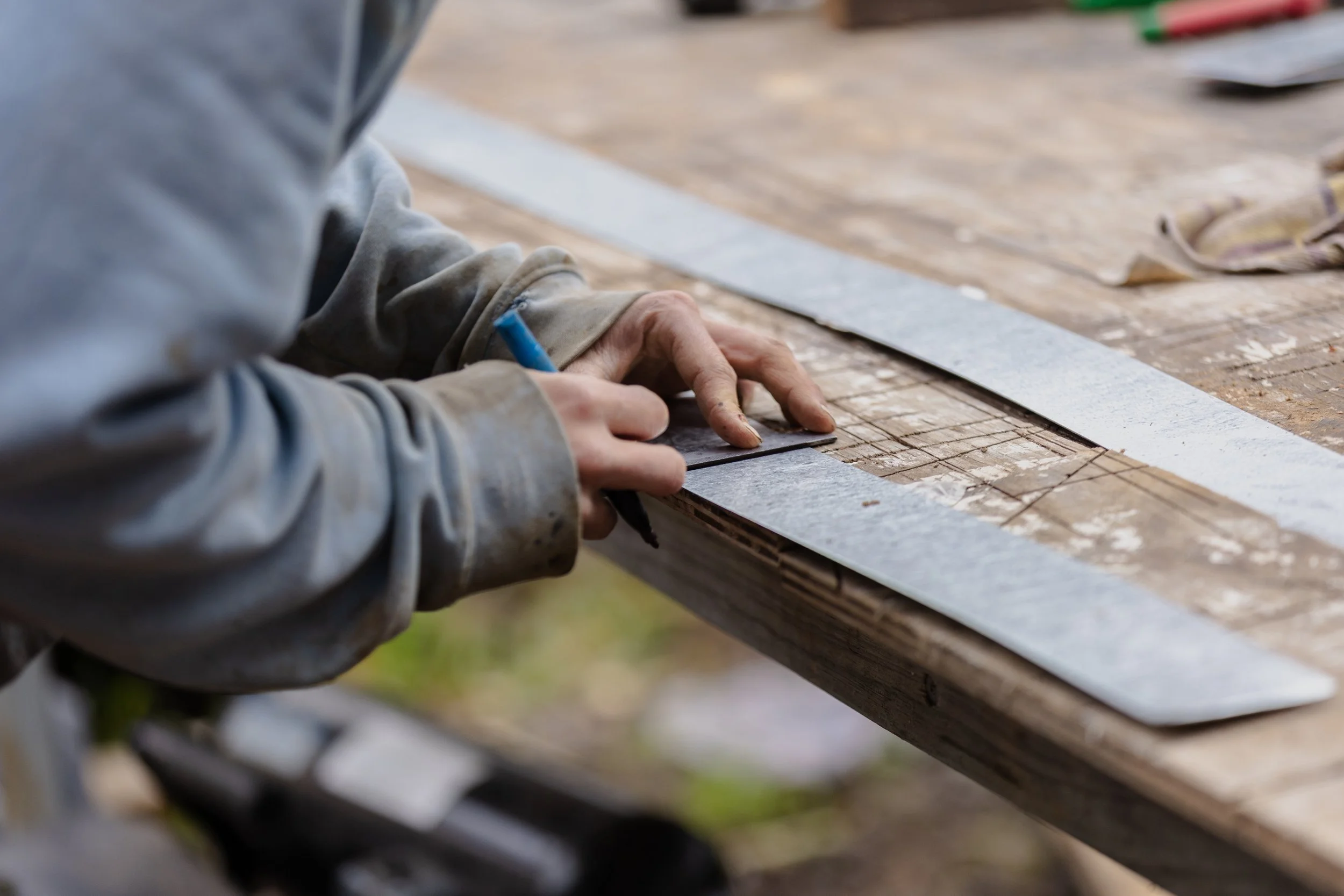 Close-up of a worker's hand measuring a wooden surface with a ruler at a construction site.