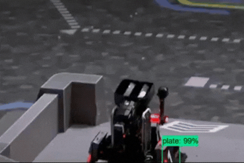 A robotic device with a screen displaying 'plate: 99%' on a miniature road scene, possibly part of an autonomous vehicle or robotic testing environment.