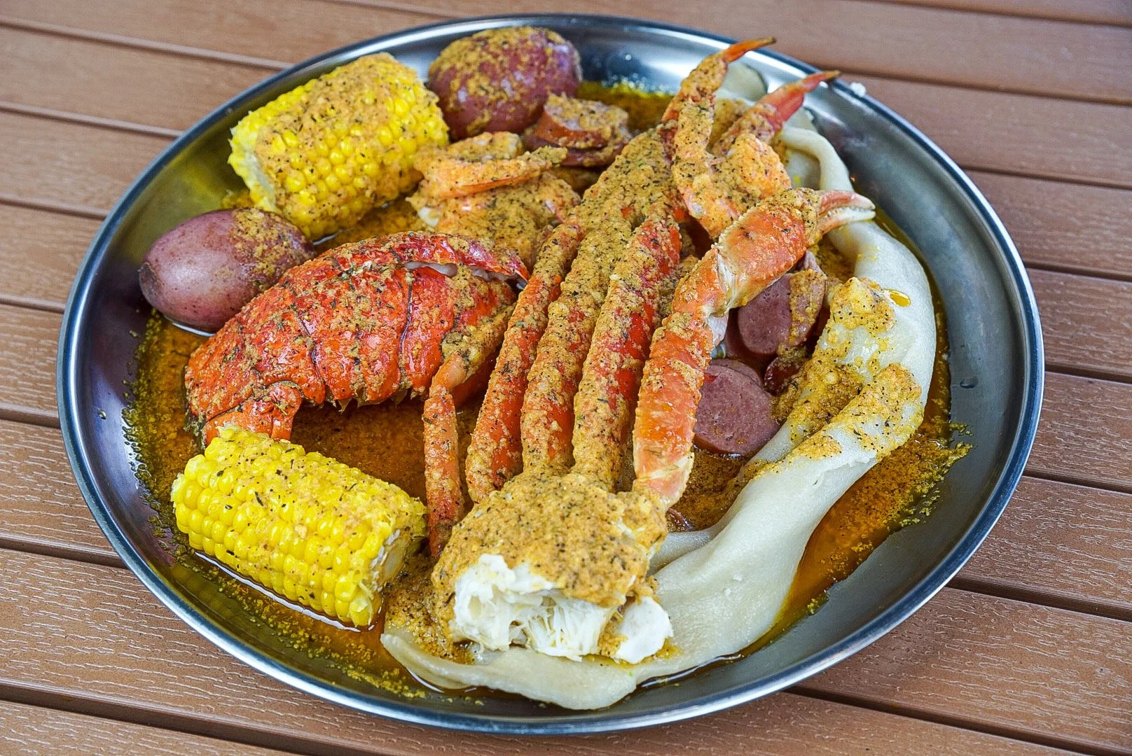 Seafood boil with lobster, shrimp, sausage, corn on the cob, potatoes, and crab in a metal tray with seasoning