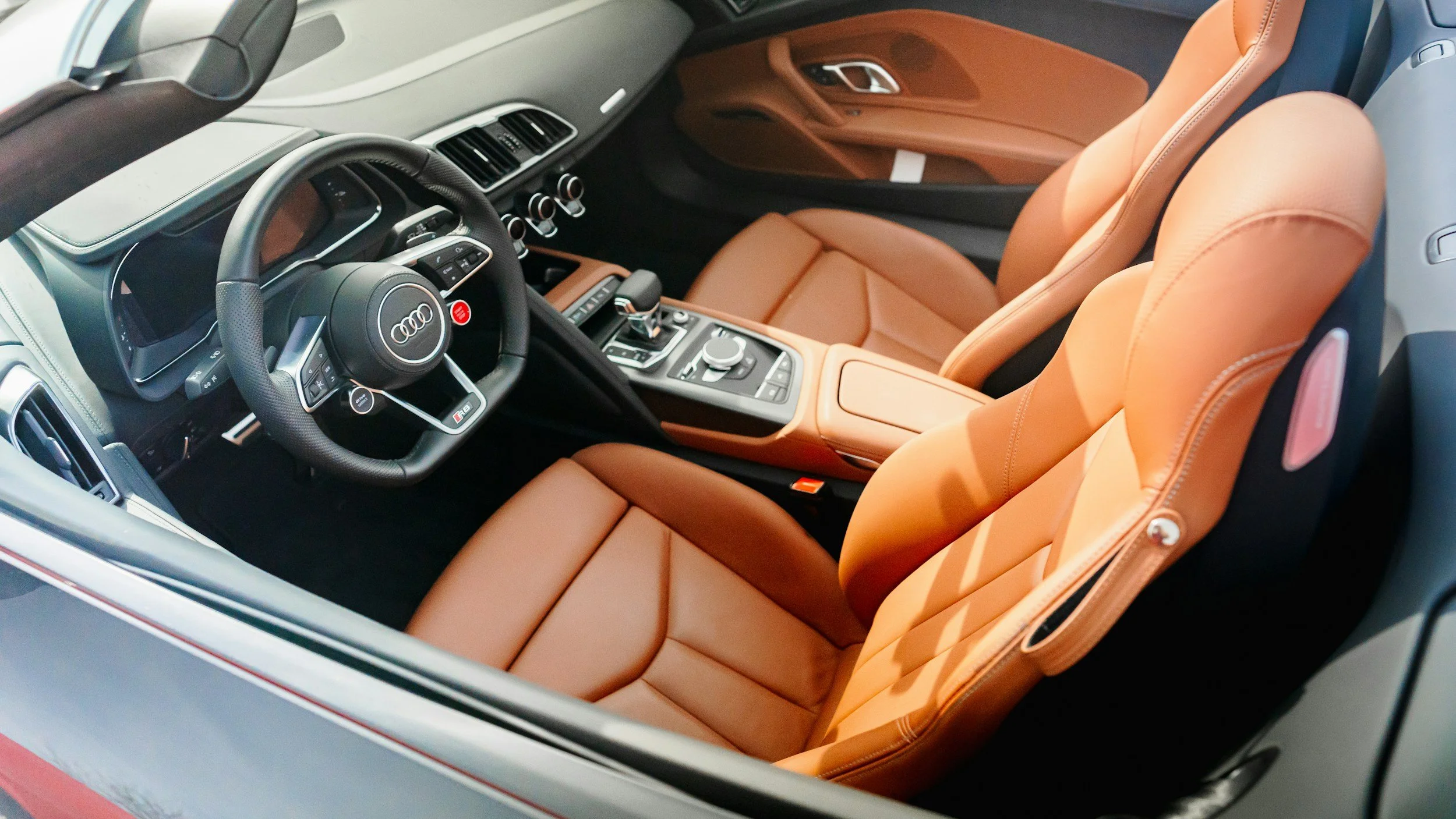 Interior of a luxury Audi sports car showcasing the steering wheel, dashboard, and tan leather seats.