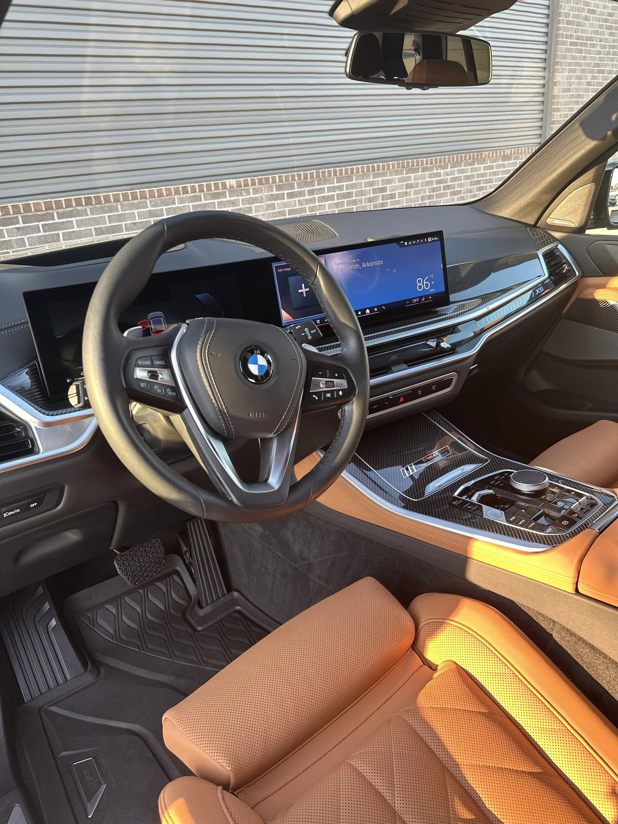 Interior of a BMW vehicle showing the steering wheel, dashboard, digital display, center console, and tan leather seats.