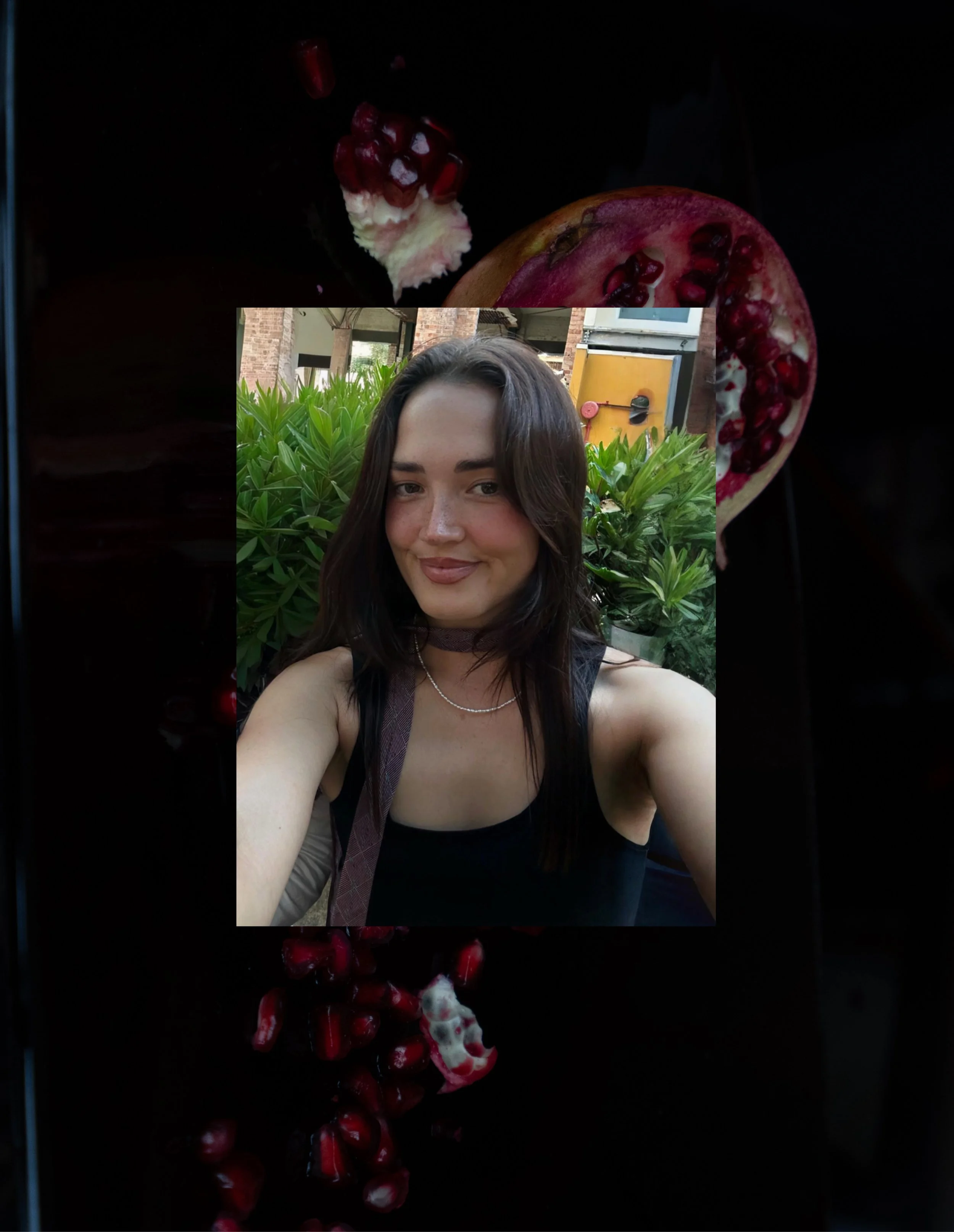 A woman taking a selfie outdoors with plants and a building in the background.