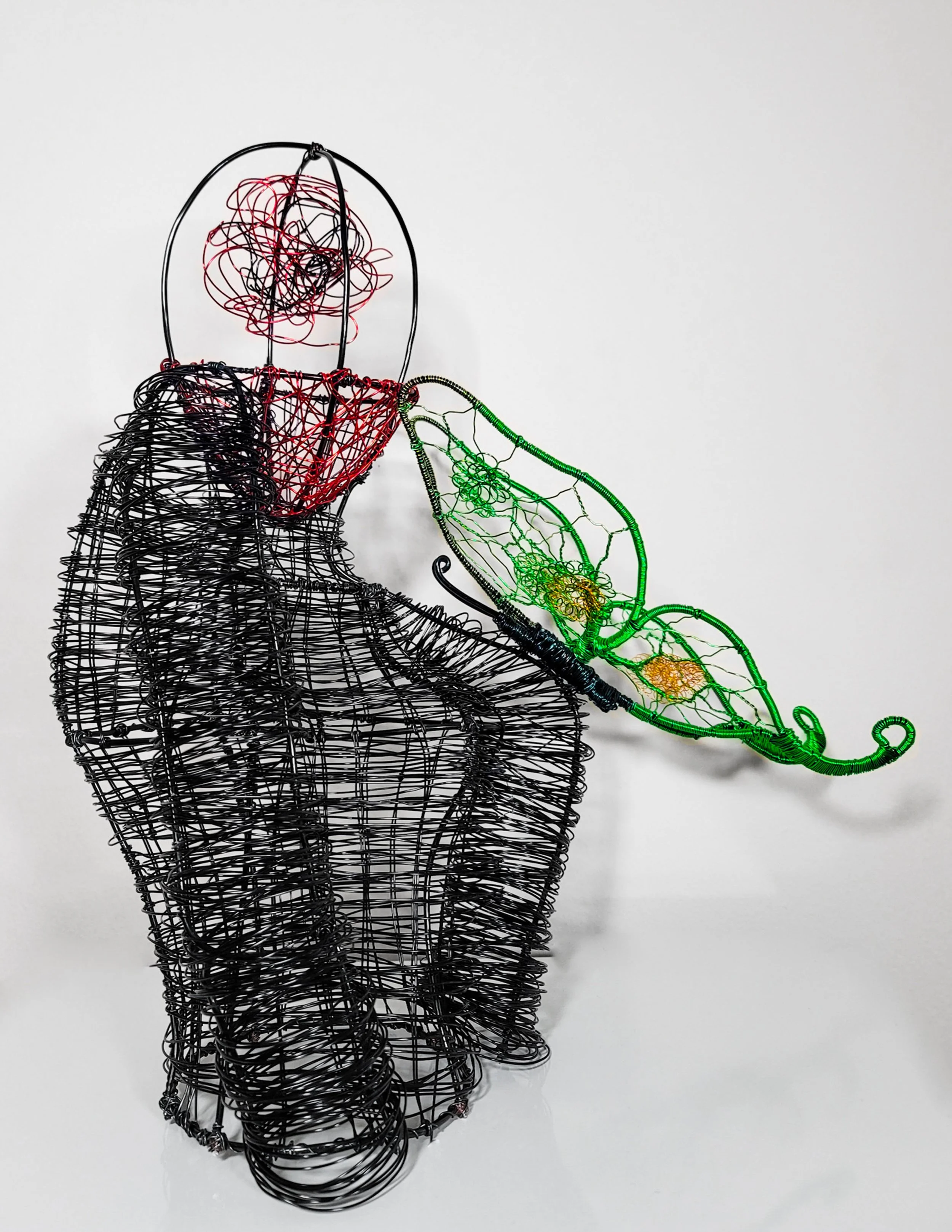 Wire sculpture of a person holding a green and yellow leaf. The sculpture is made of black, red, and green wire on a white background.