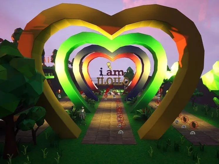 Colorful heart-shaped arches creating a tunnel effect, with a pathway leading through them. The scene includes trees, grass, and decorative lighting, with a sign in the background that reads "I am ILOILO".