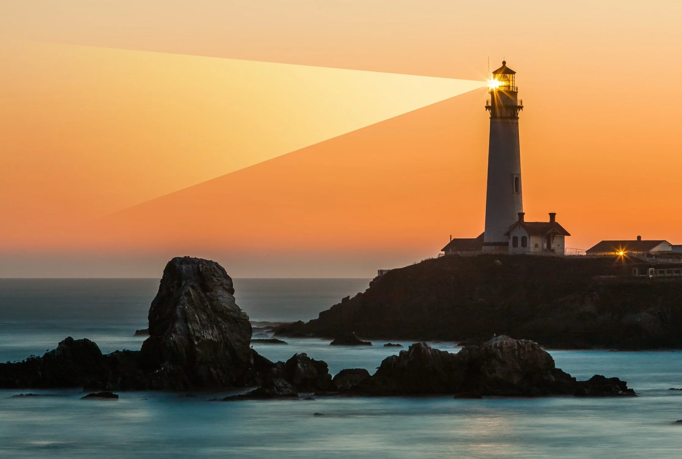 A lighthouse on a coastal cliff at sunset with a bright beacon, rocks in the ocean, and a colorful sky in shades of orange and yellow.
