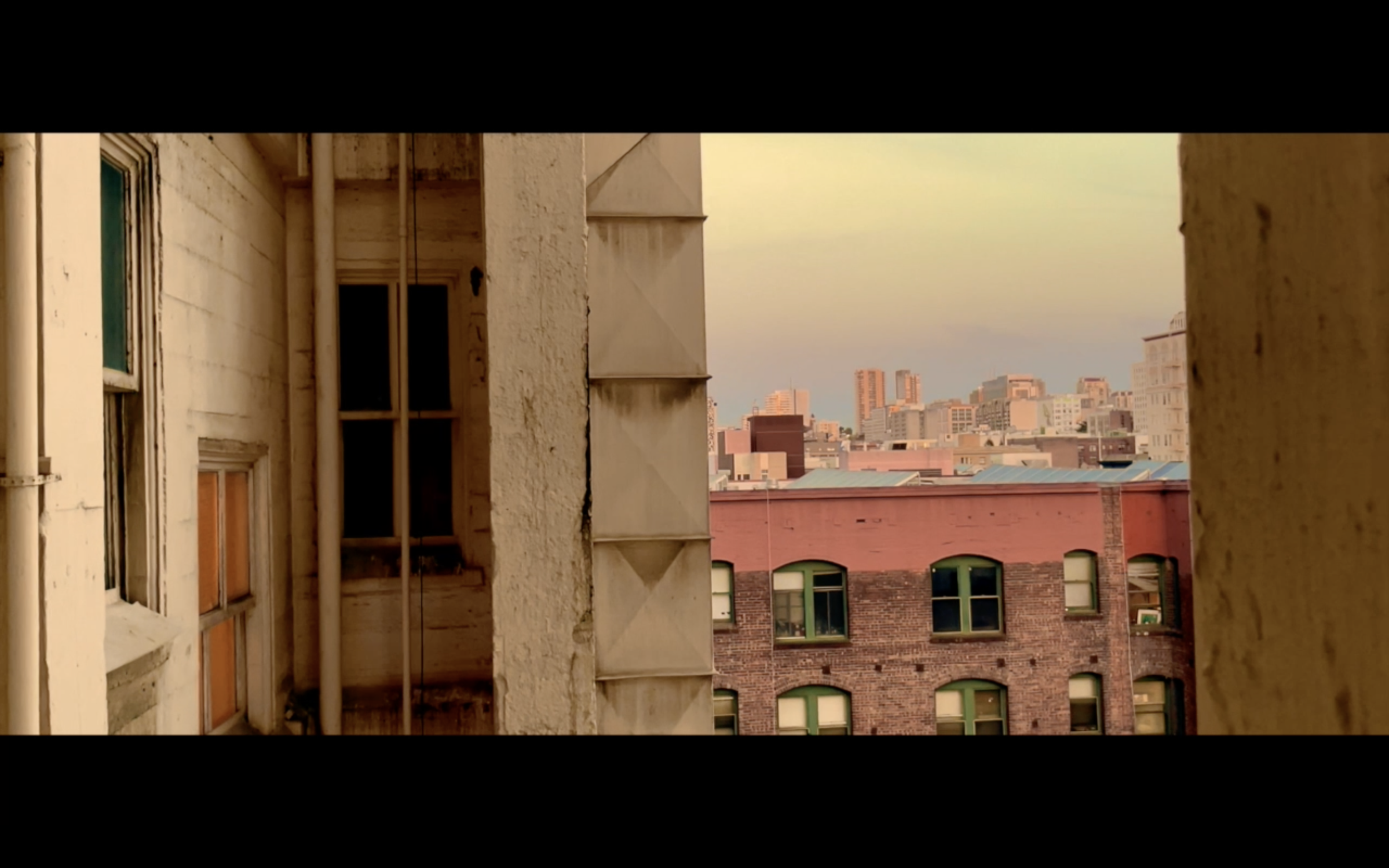 View of city buildings seen through a narrow gap between two older brick and concrete buildings at sunset.