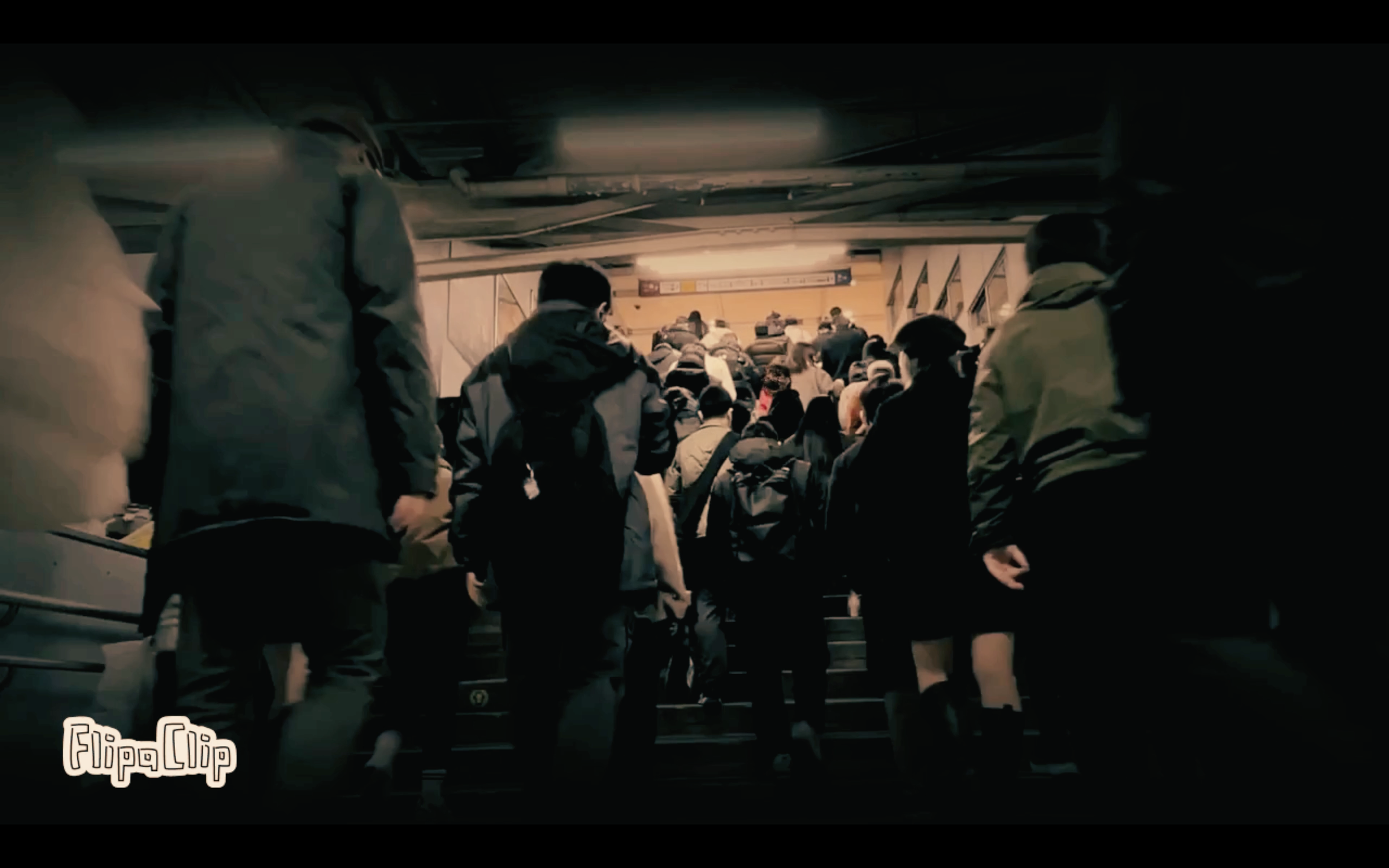 Crowded staircase at an airport or train station with people ascending and descending the stairs, some with backpacks and bags.