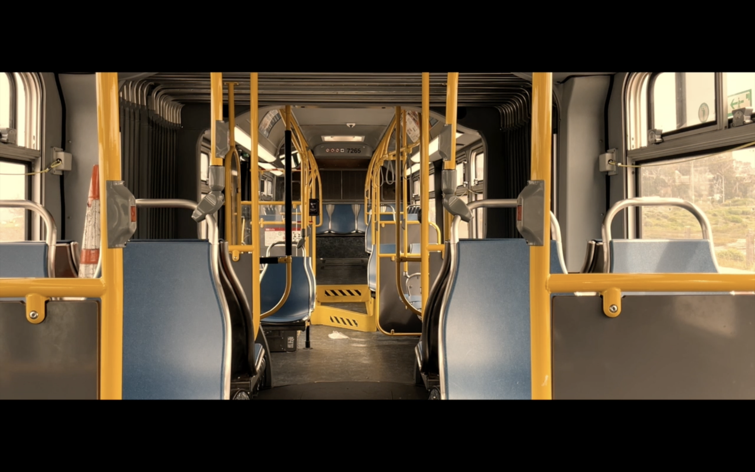 Interior of an empty public bus with blue seats, yellow handrails, and large windows.