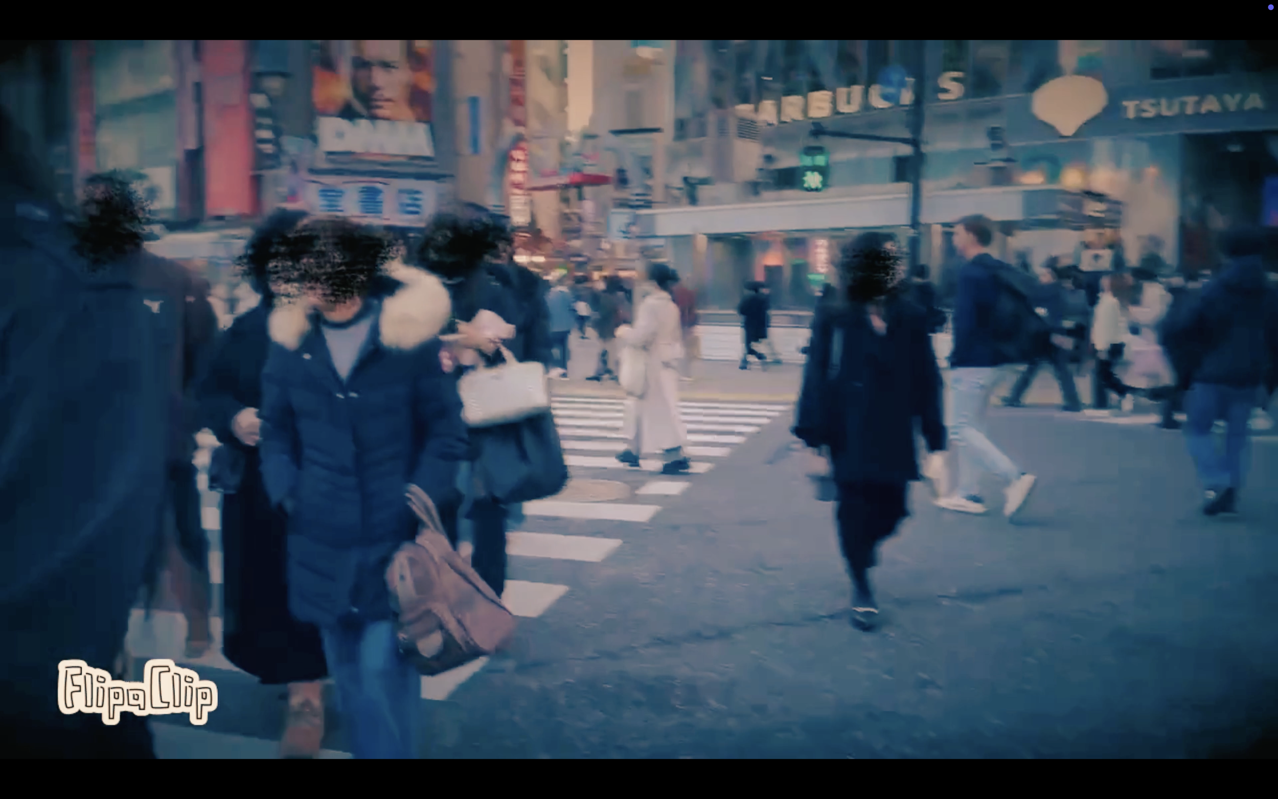People crossing a busy urban street in Japan, with advertisements on buildings and a green pedestrian signal.