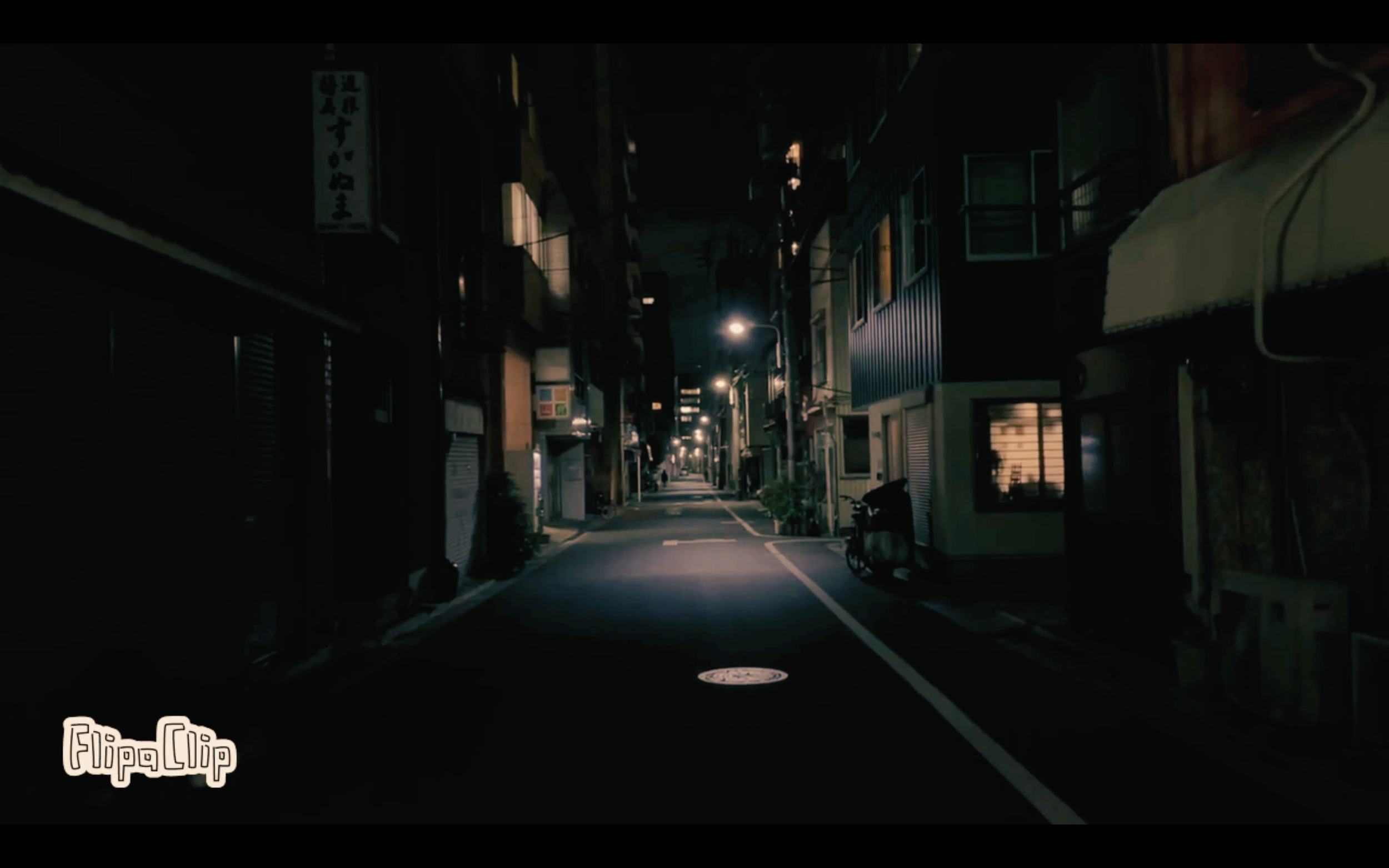 Empty narrow city street at night with streetlights and buildings on both sides.