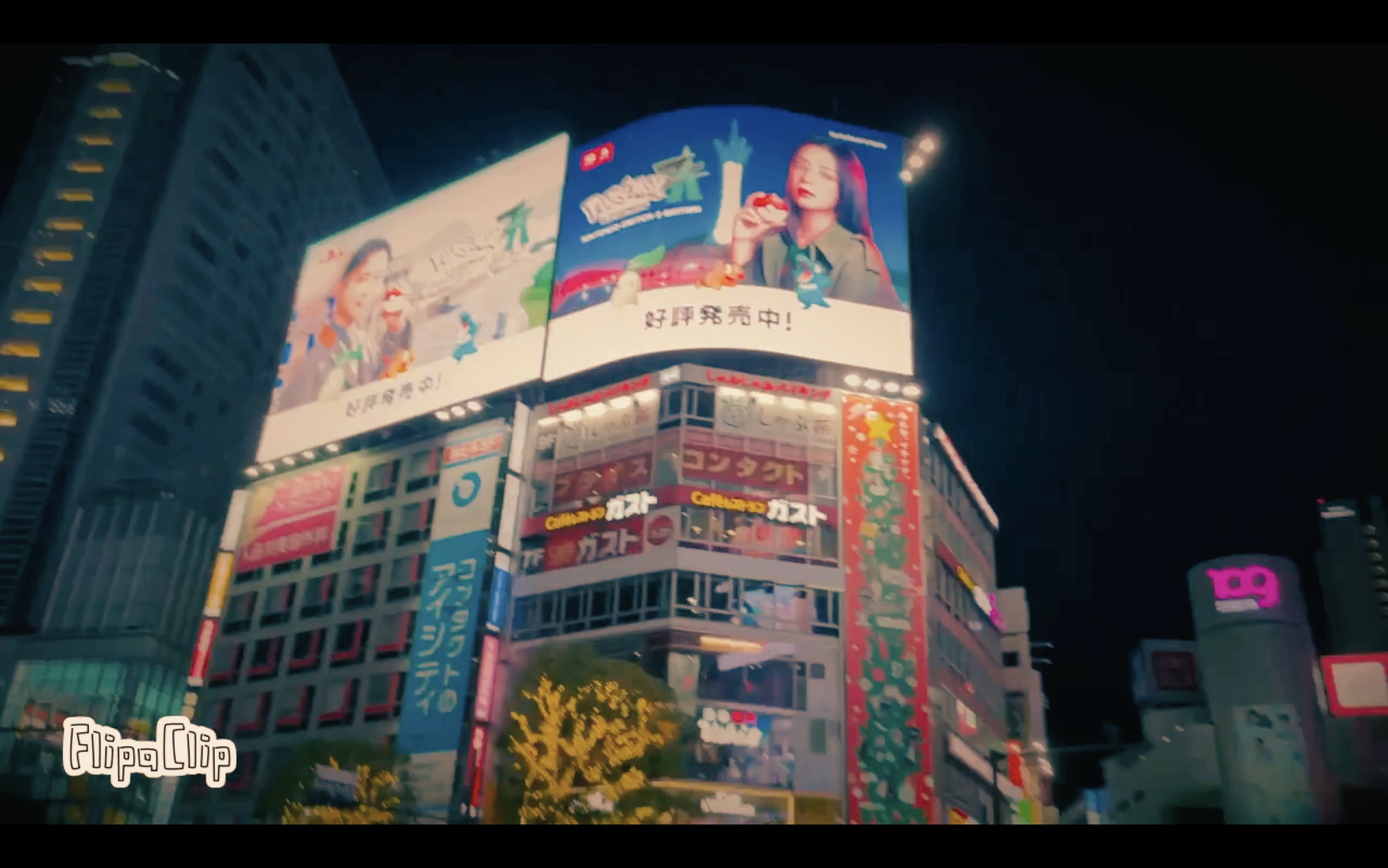 Nighttime cityscape with bright billboards and neon signs, including a large billboard featuring a woman eating a strawberry and smaller billboards with Japanese or Chinese characters on a multi-story building.