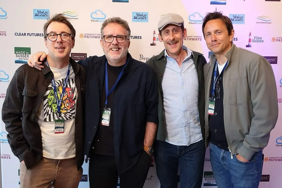 Four men standing together at an event with a background displaying logos for Maize & Grace, CloudConnex, Sussex Film Festival, and other organizations. They are smiling, with three wearing conference badges around their necks.