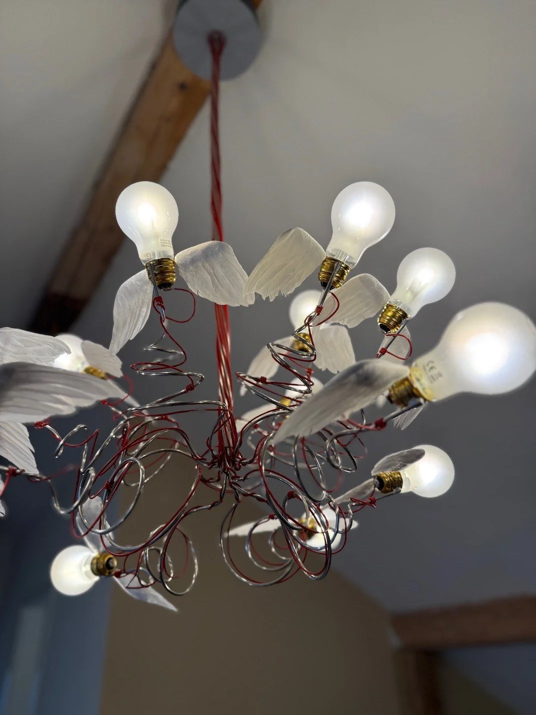 Hängelampe mit LED-Glühbirnen, weissen Flügeln und roten Drähten, an der Decke an einer Holzleiste befestigt.