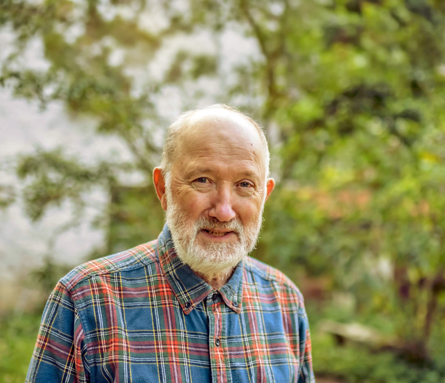 Frank Carlson, Künstler, trägt ein bunt kariertes Hemd und steht im Grünen.