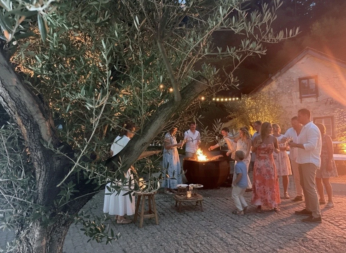 Menschen feiern draussen bei einem Grillabend in warmem Licht, umgeben von Bäumen und einer alten Steinmauer.