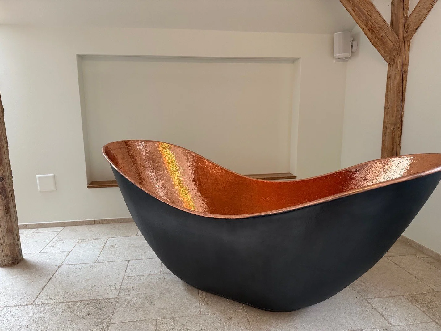 Eine moderne Badewanne mit schwarzer Aussenseite und kupferner Innenseite steht in einem Raum mit schieferfarbenem Boden und weissen Wänden.
