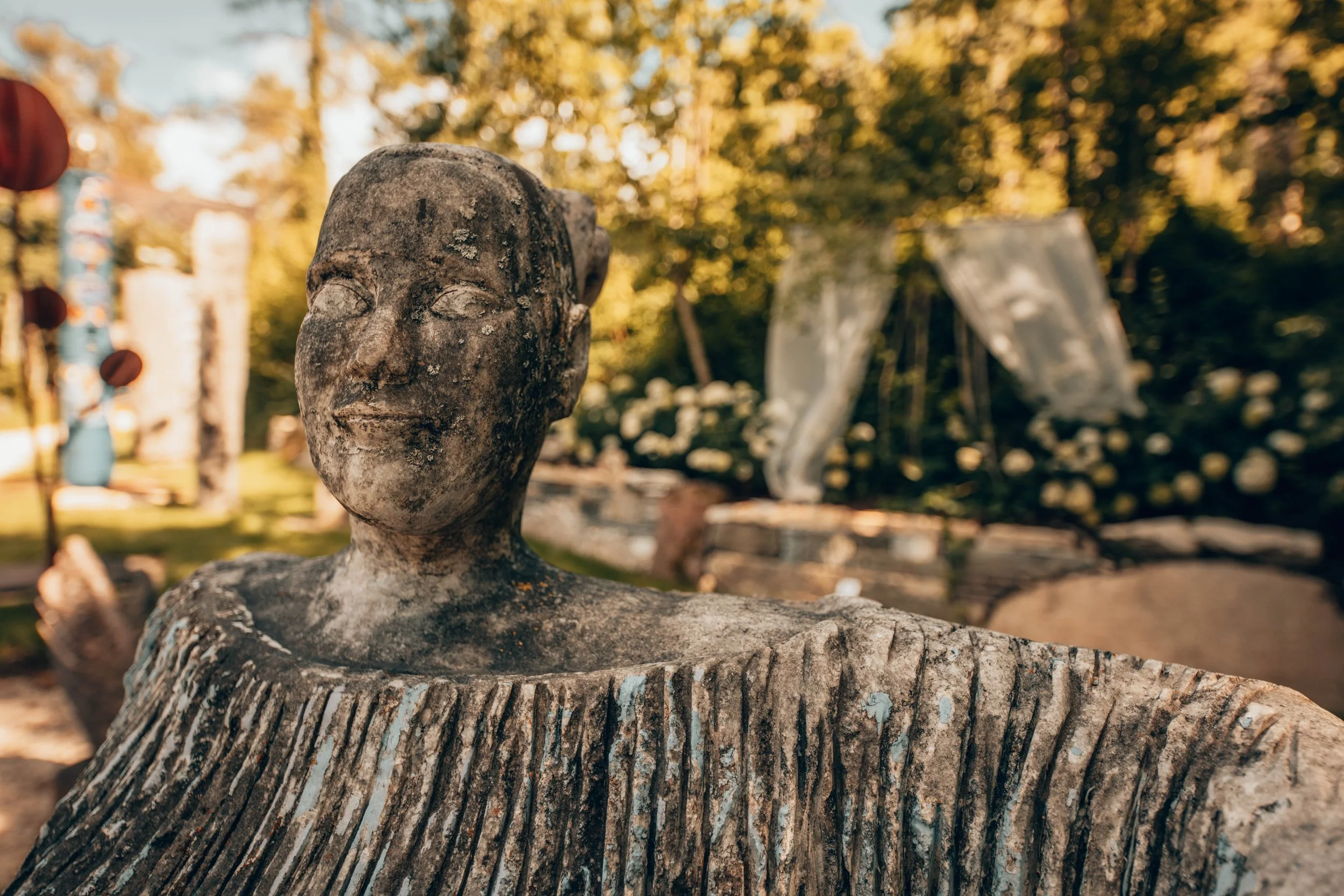 Steinskulptur eines lachenden Menschenkopfes im Freien.