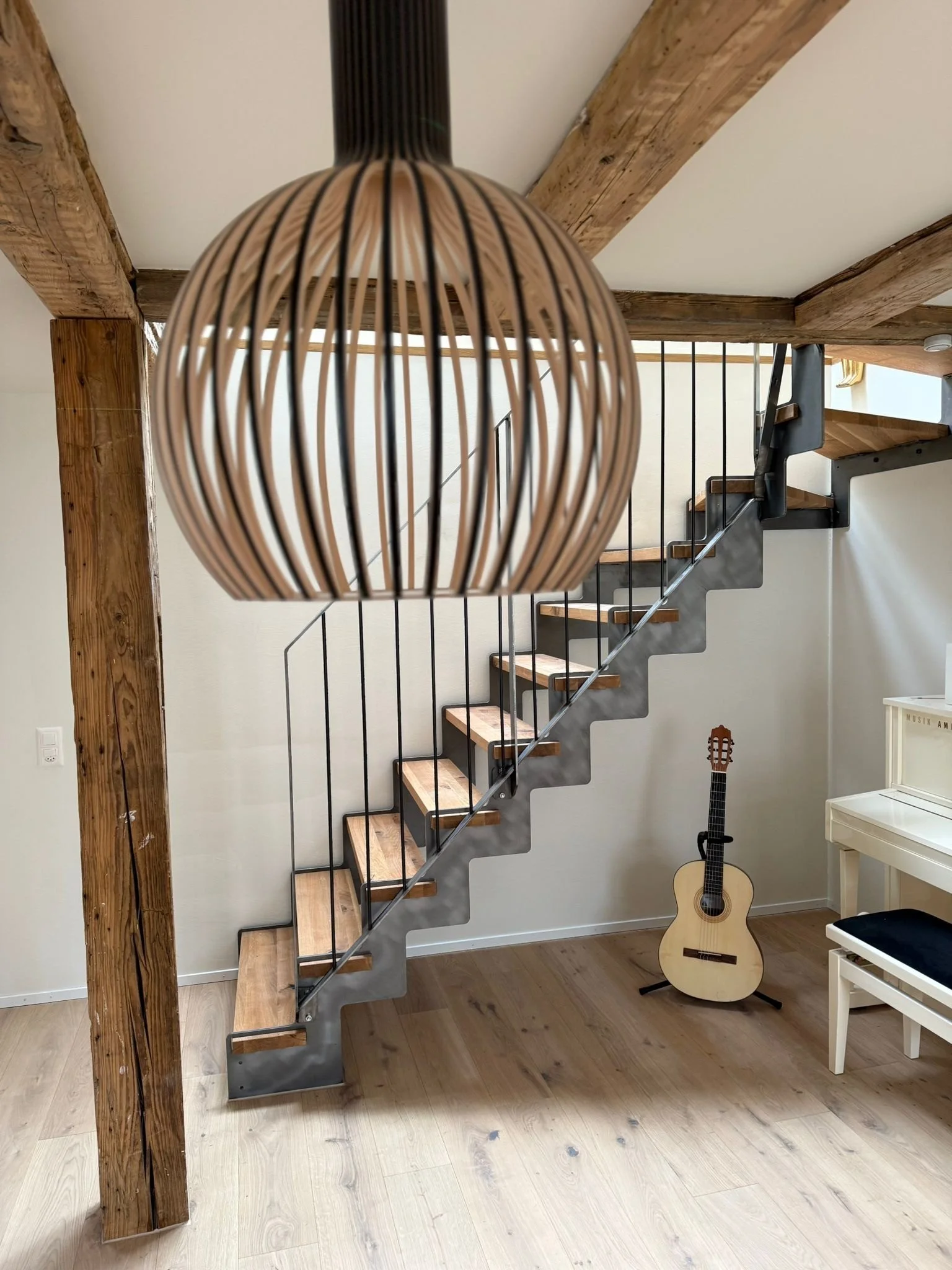 Innenraum mit einer modernen Holztreppe, einer Gitarre, einem weissen Klavier und einer Lampe aus Holz.