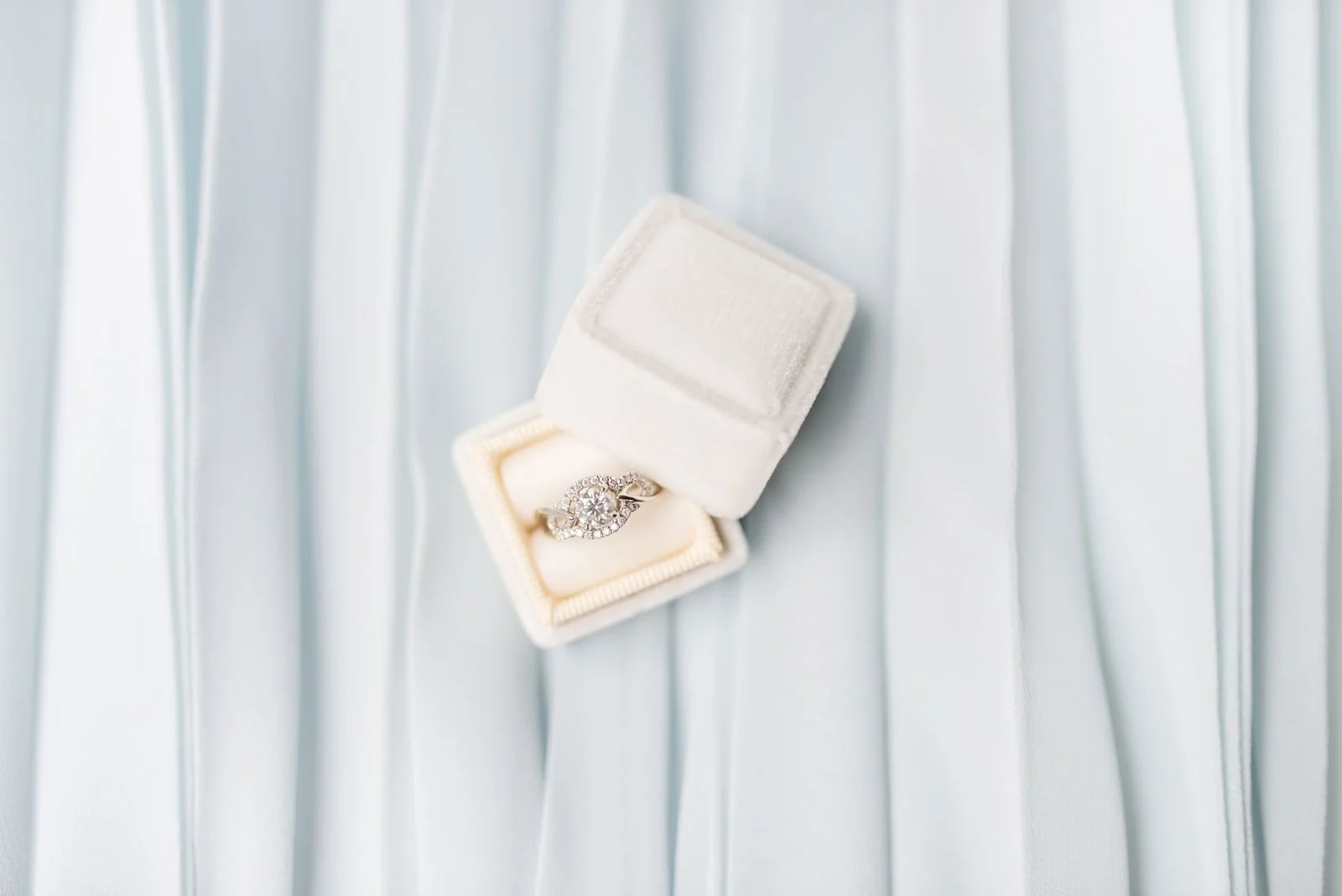 Close-up of a diamond engagement ring in a velvet box on soft pale fabric