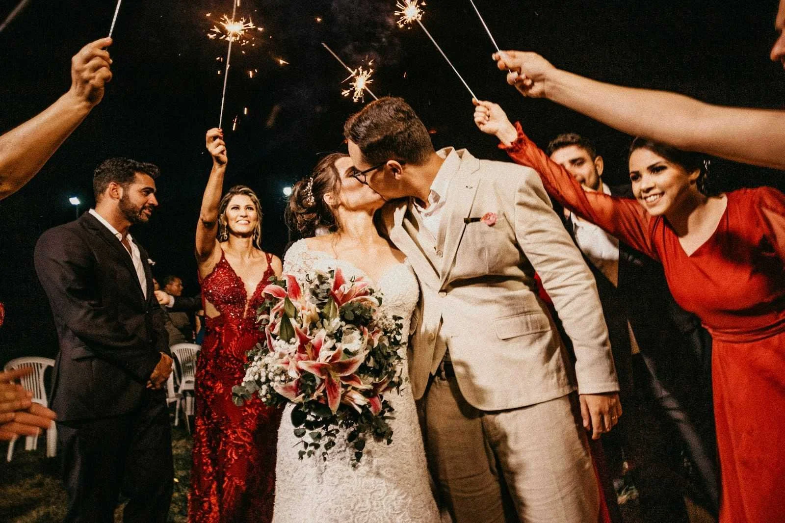 Bride and groom kiss surrounded by wedding guests holding sparklers during a countryside evening celebration in Lancashire