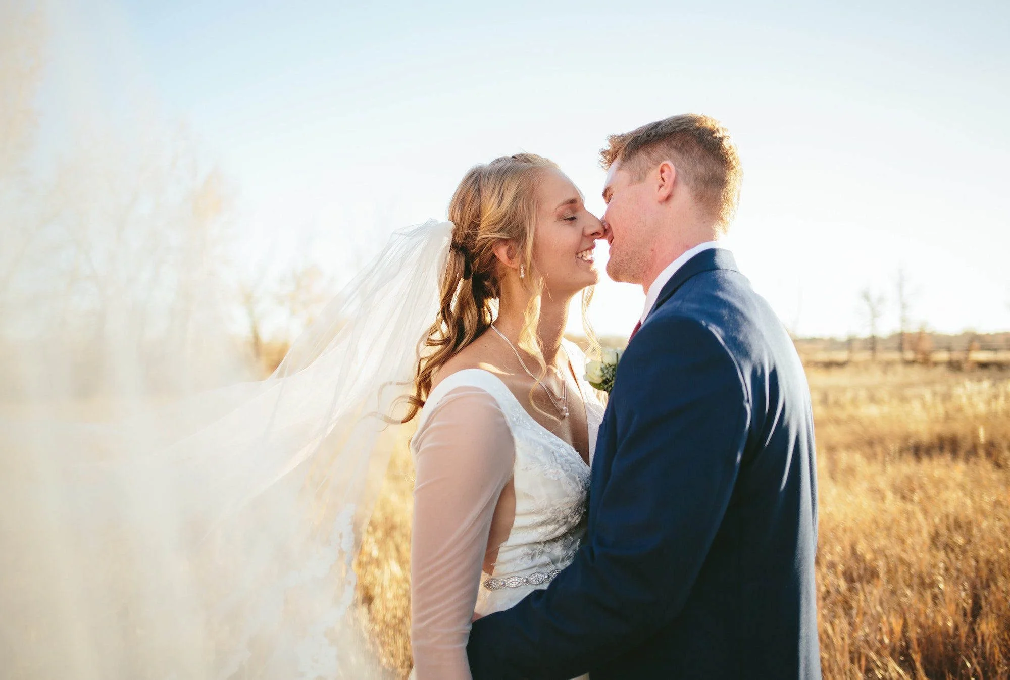 Bride and groom sharing a joyful moment during golden hour, with her veil flowing in the breeze, captured in a natural Stockport countryside setting