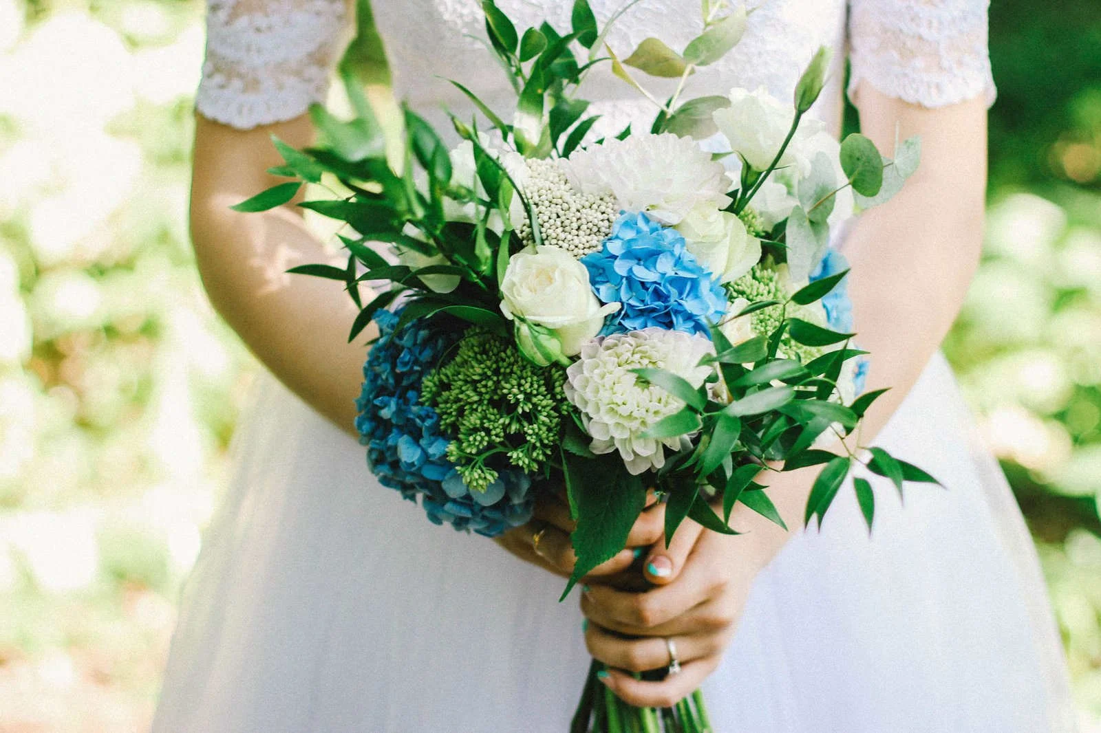 Bride holding a vibrant bouquet of blue hydrangeas and white roses on her wedding day