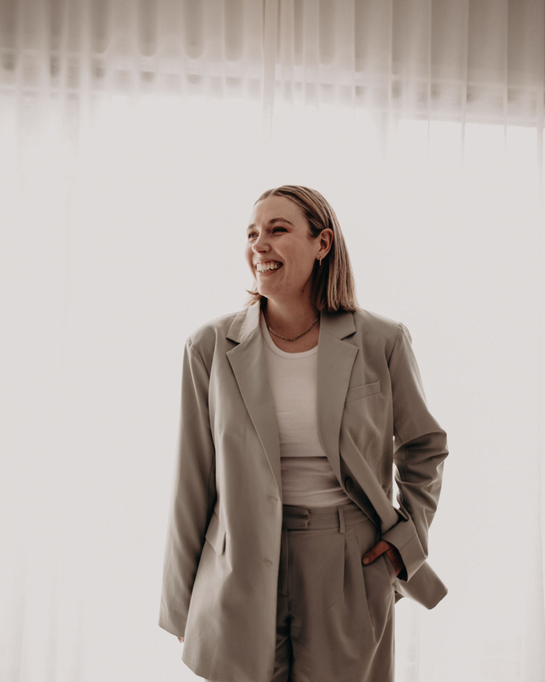 A woman in a beige suit smiling and standing against a light background.